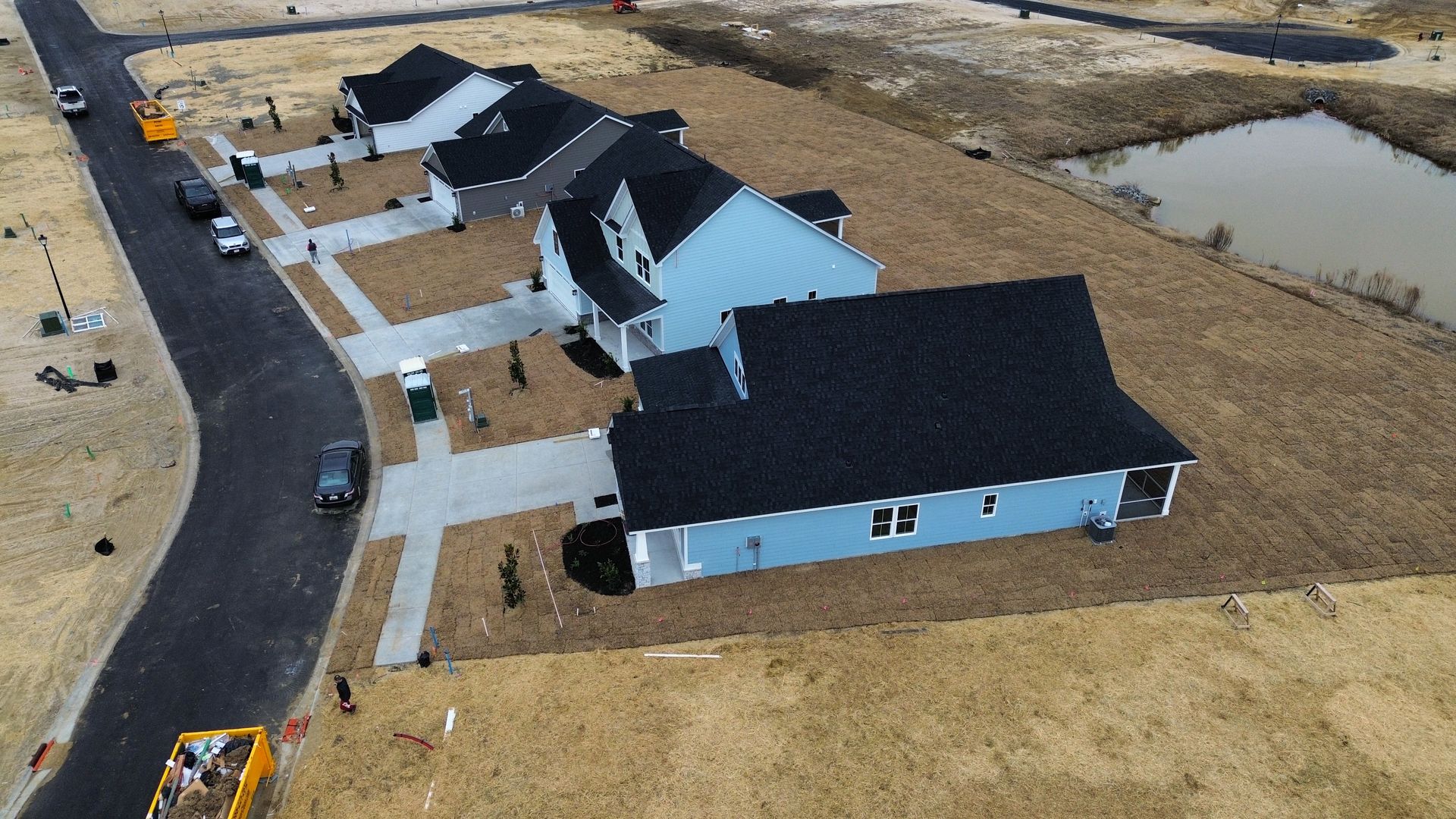 Aerial view of several blue houses with black roofs and gray driveways under construction.