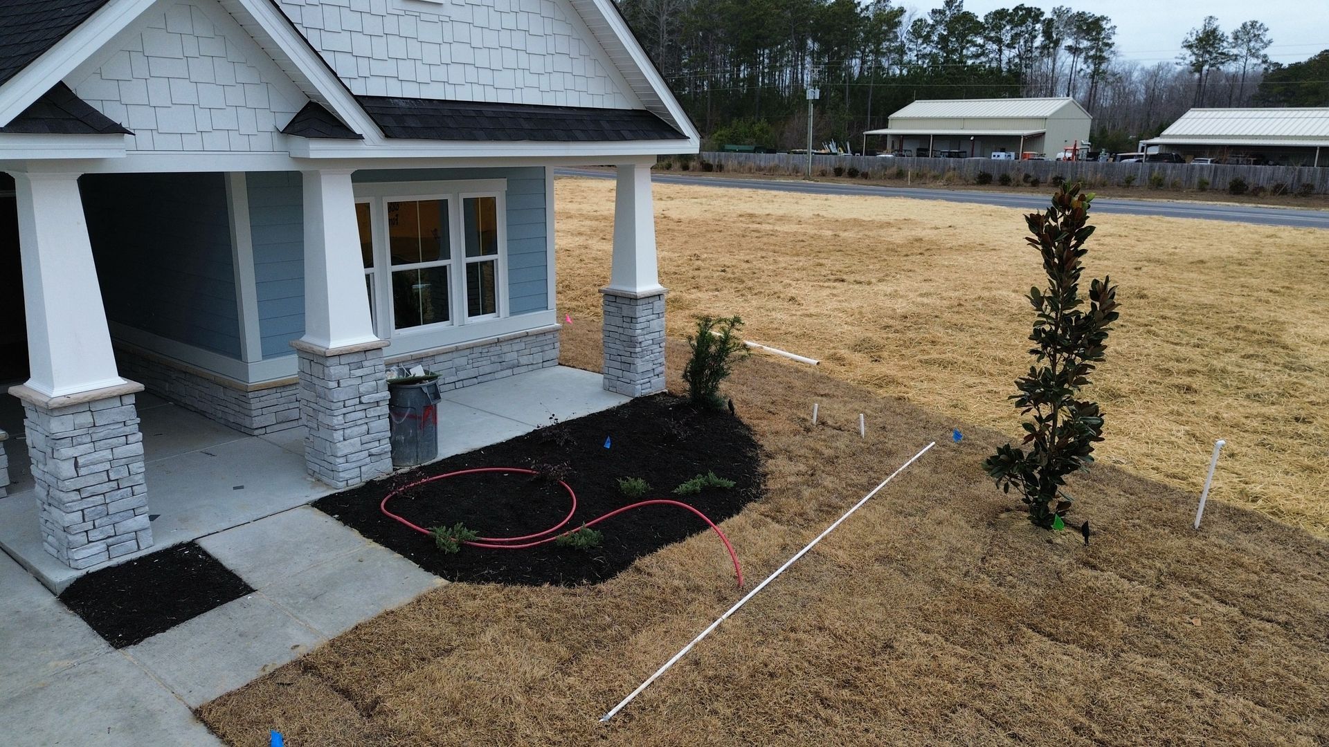 House with blue siding, gray columns, and a small landscaped bed in front.