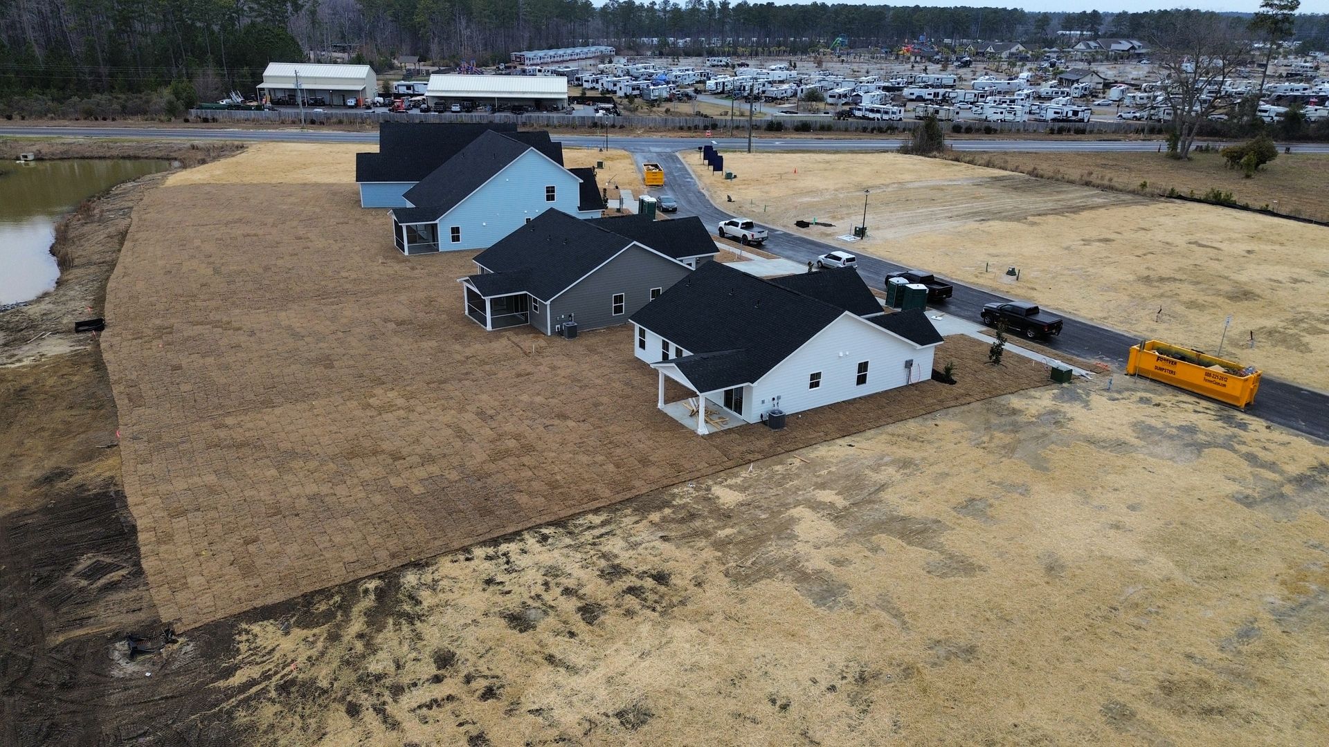 Houses under construction, mostly neutral colors, in a field, with a yellow truck on the road.