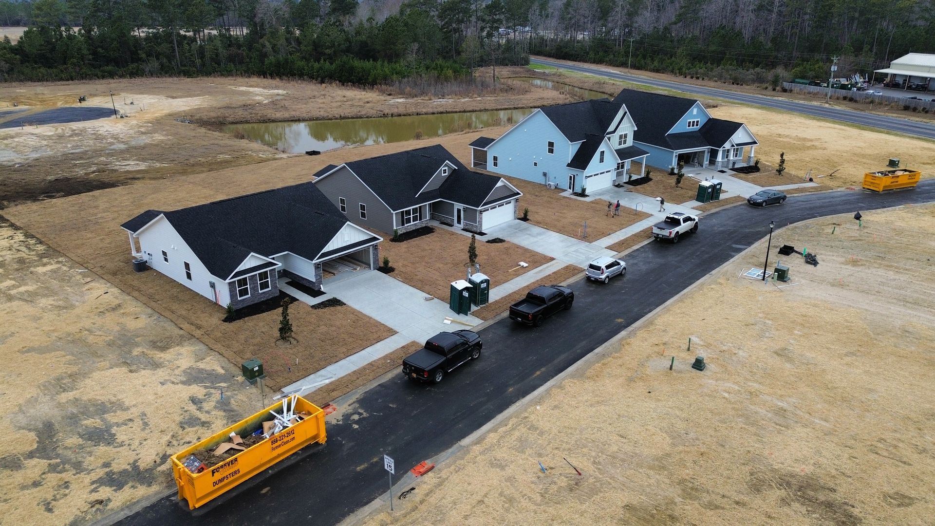 Aerial view of new houses on a road, with construction vehicles and cars present.