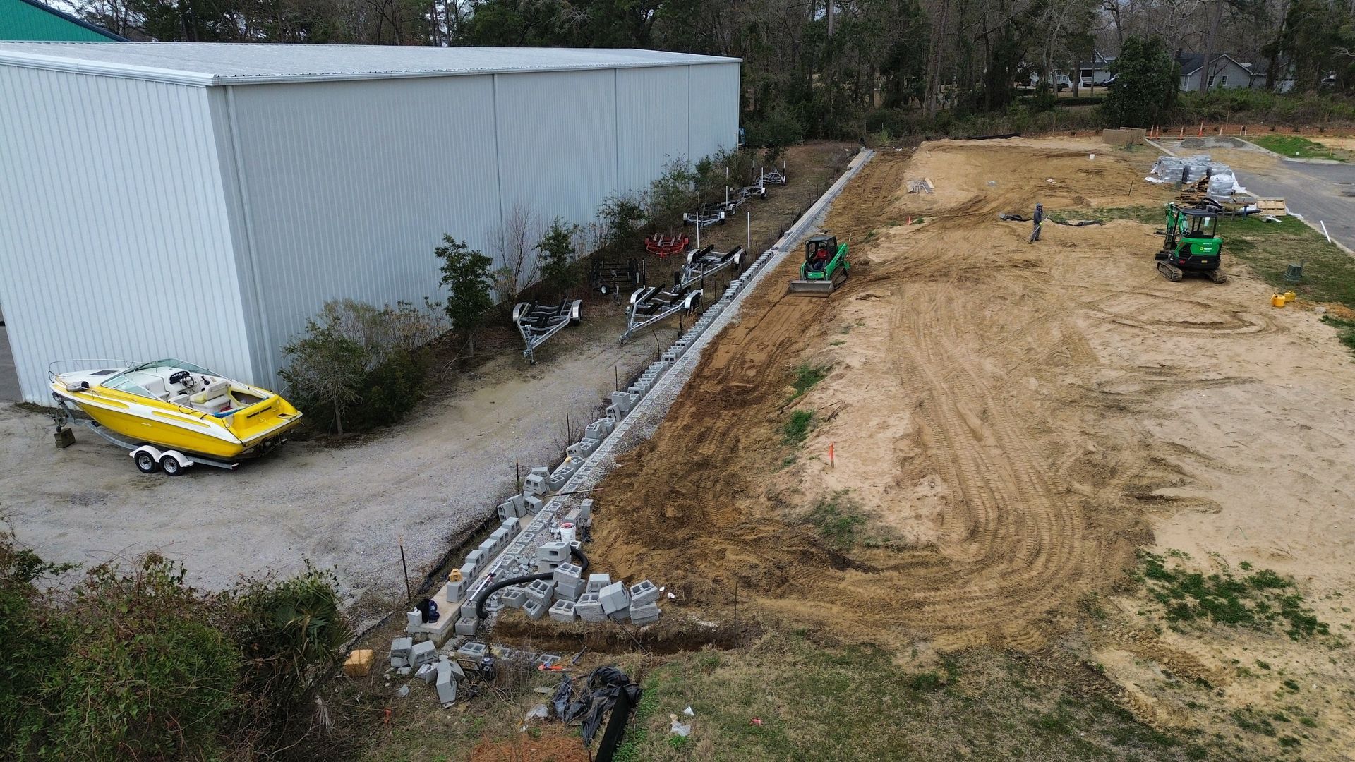 Construction site with a building, retaining wall, and machinery. A yellow boat sits nearby.