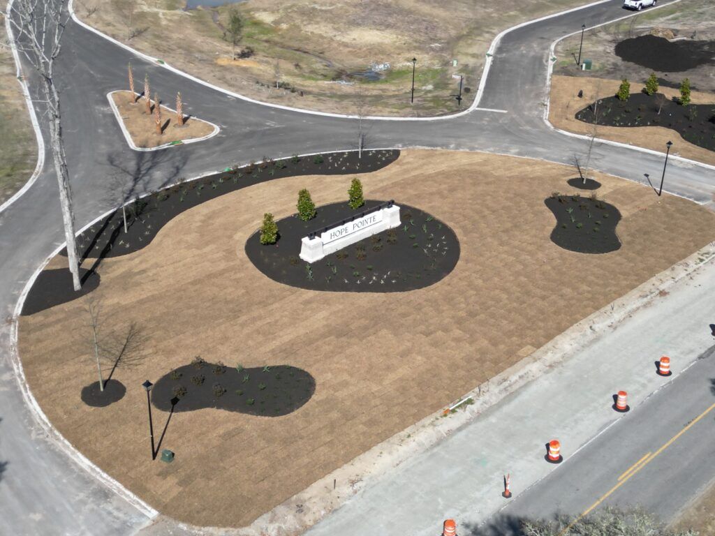 Aerial view of a landscaped roundabout with a sign, surrounded by roads and brown grass.