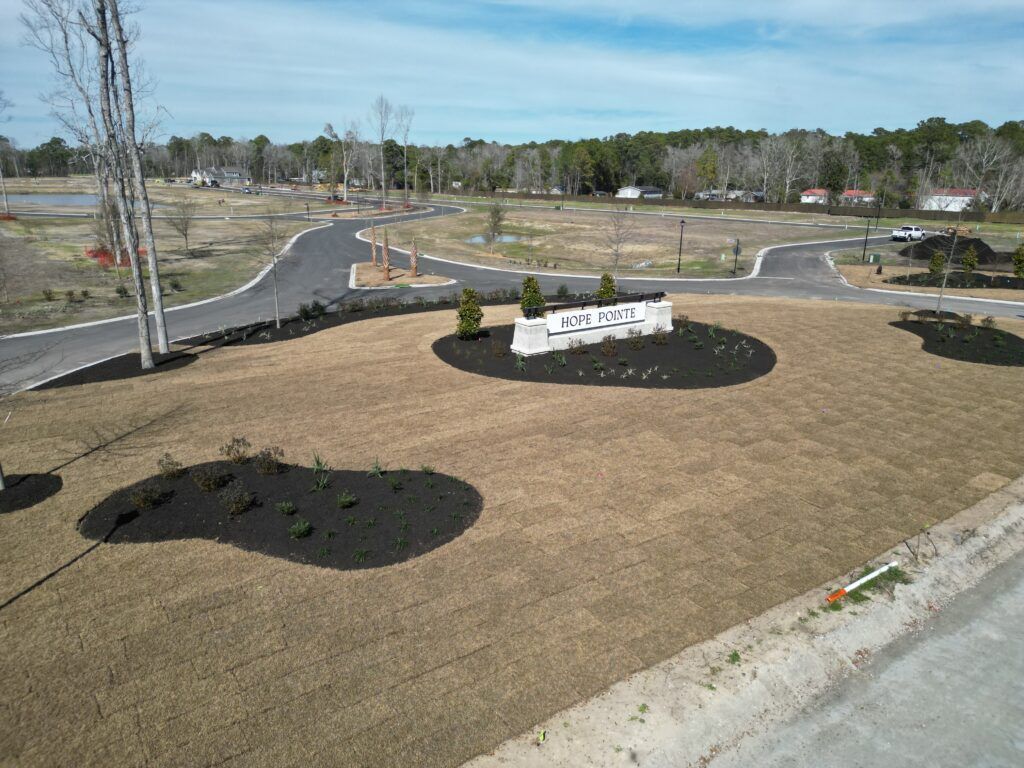 Entrance sign for a development with new asphalt roads, landscaped with mulch and grass.