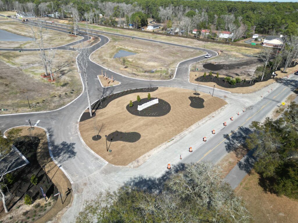 Aerial view of a newly constructed road intersection with a roundabout, landscaping, and surrounding greenery.