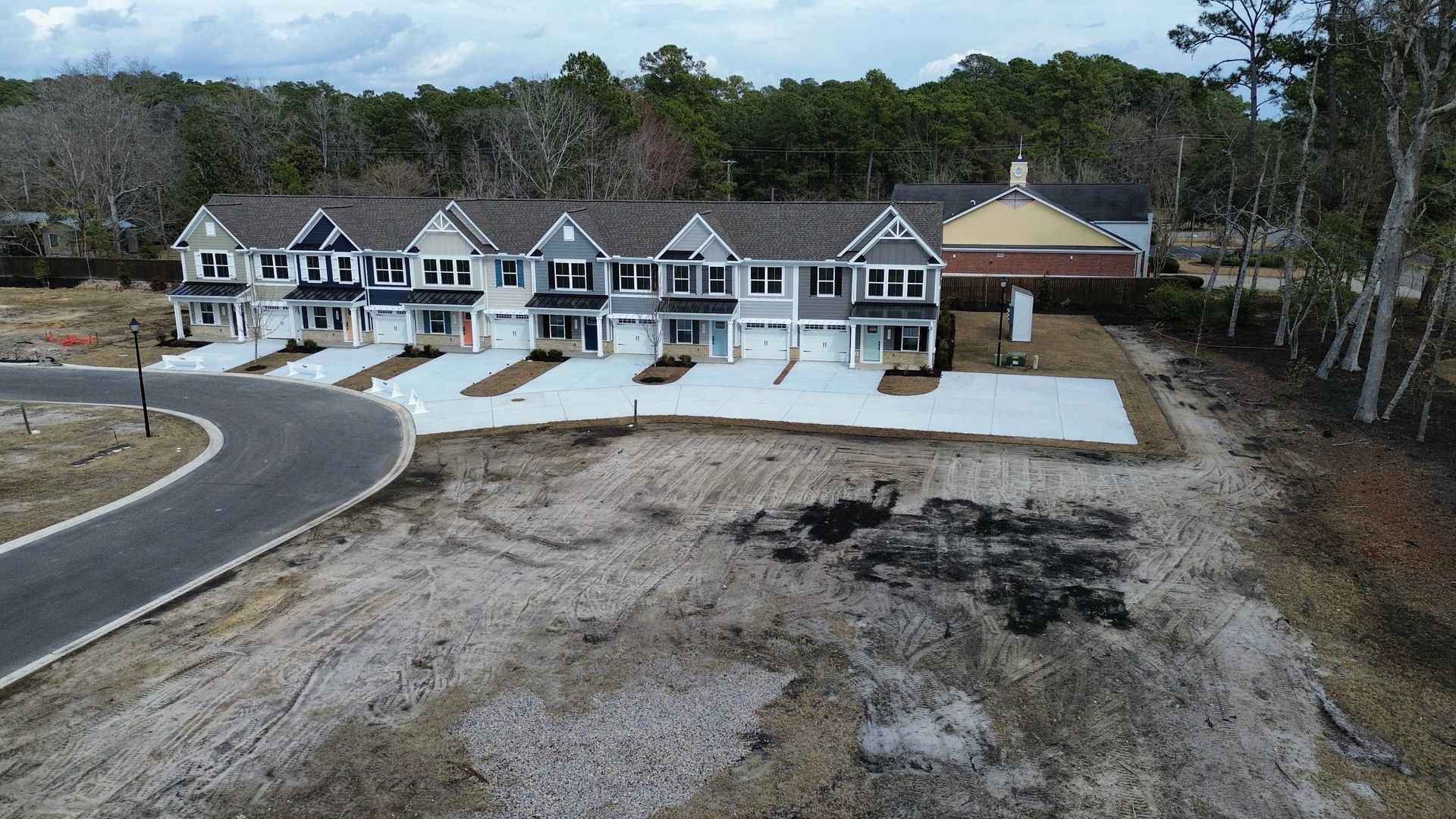 Row of newly built townhouses with varying colored facades, next to a street, on a cleared lot.