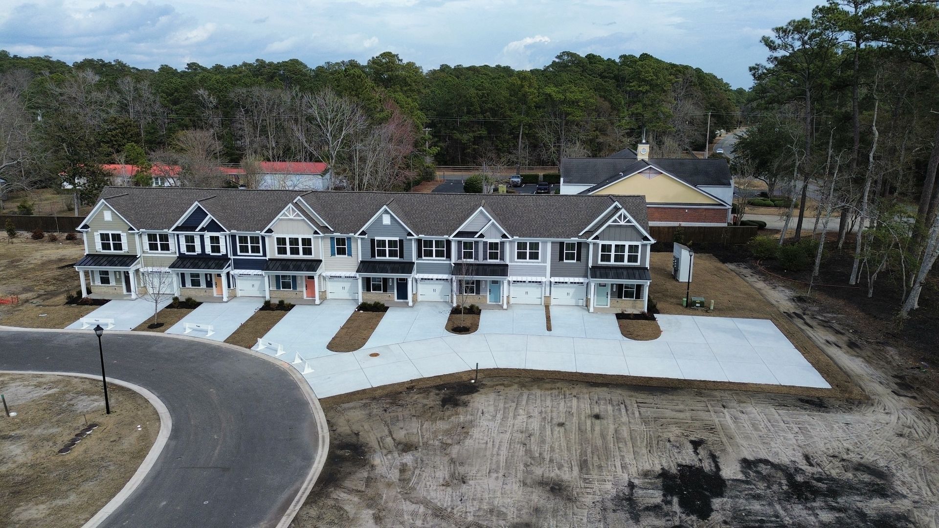 Row of new townhouses with gray and blue siding, concrete driveways, and surrounding trees.