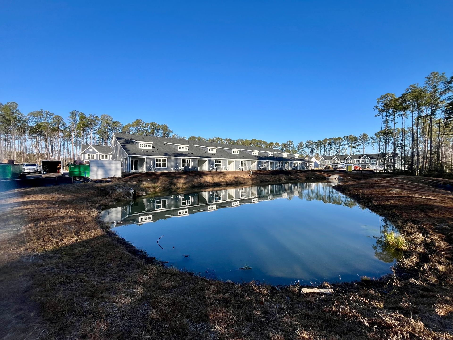 Row of new townhouses with pond in front, blue sky, trees.