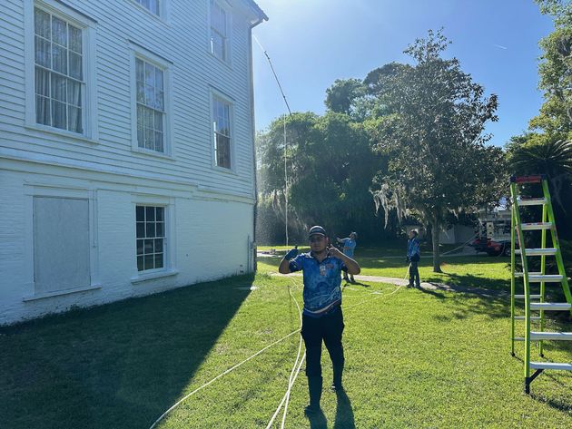 Person standing on a grassy lawn beside a white building, with a ladder and trees in bright sunlight.