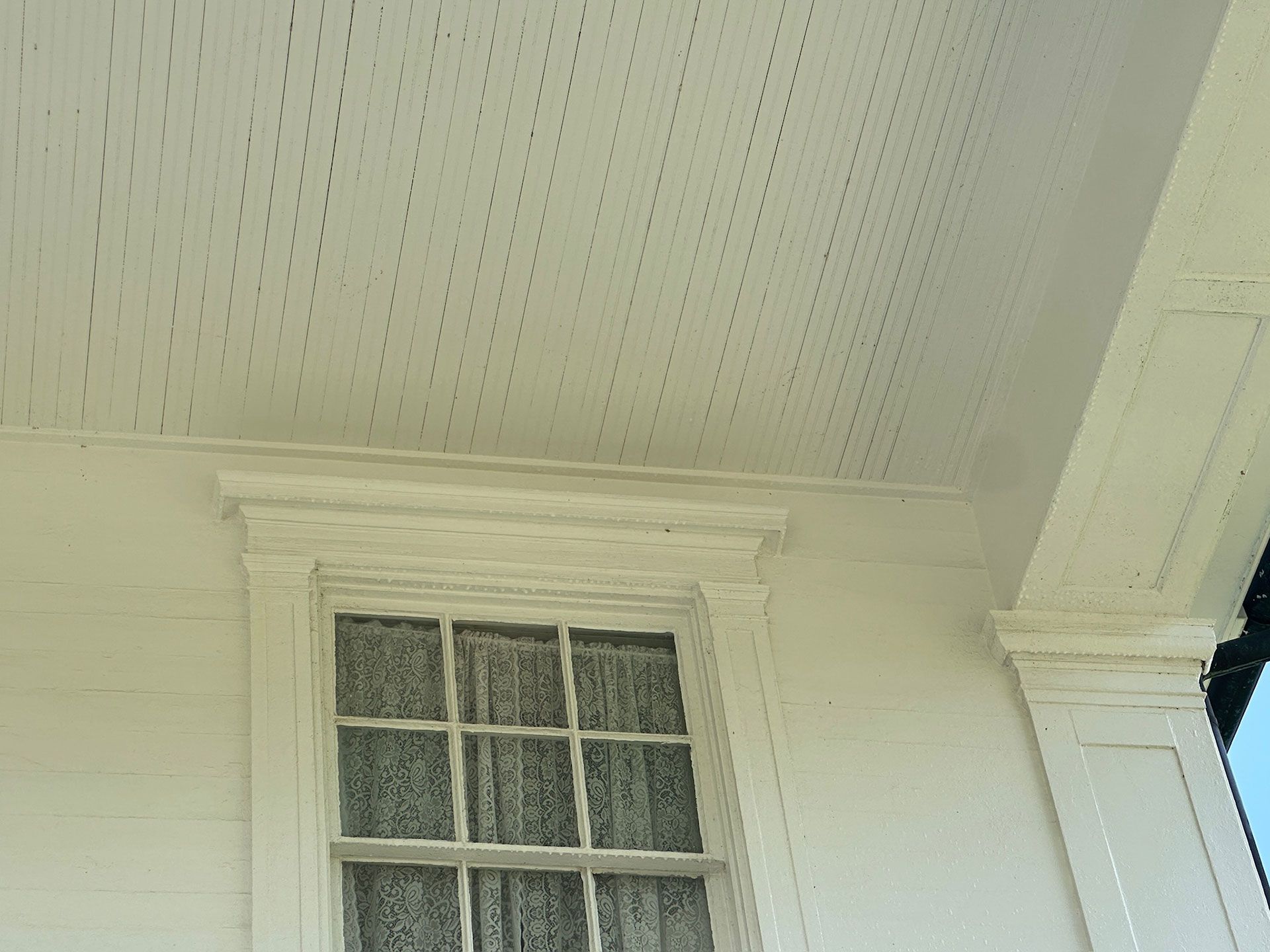 White exterior wall with a small paned window under a porch ceiling