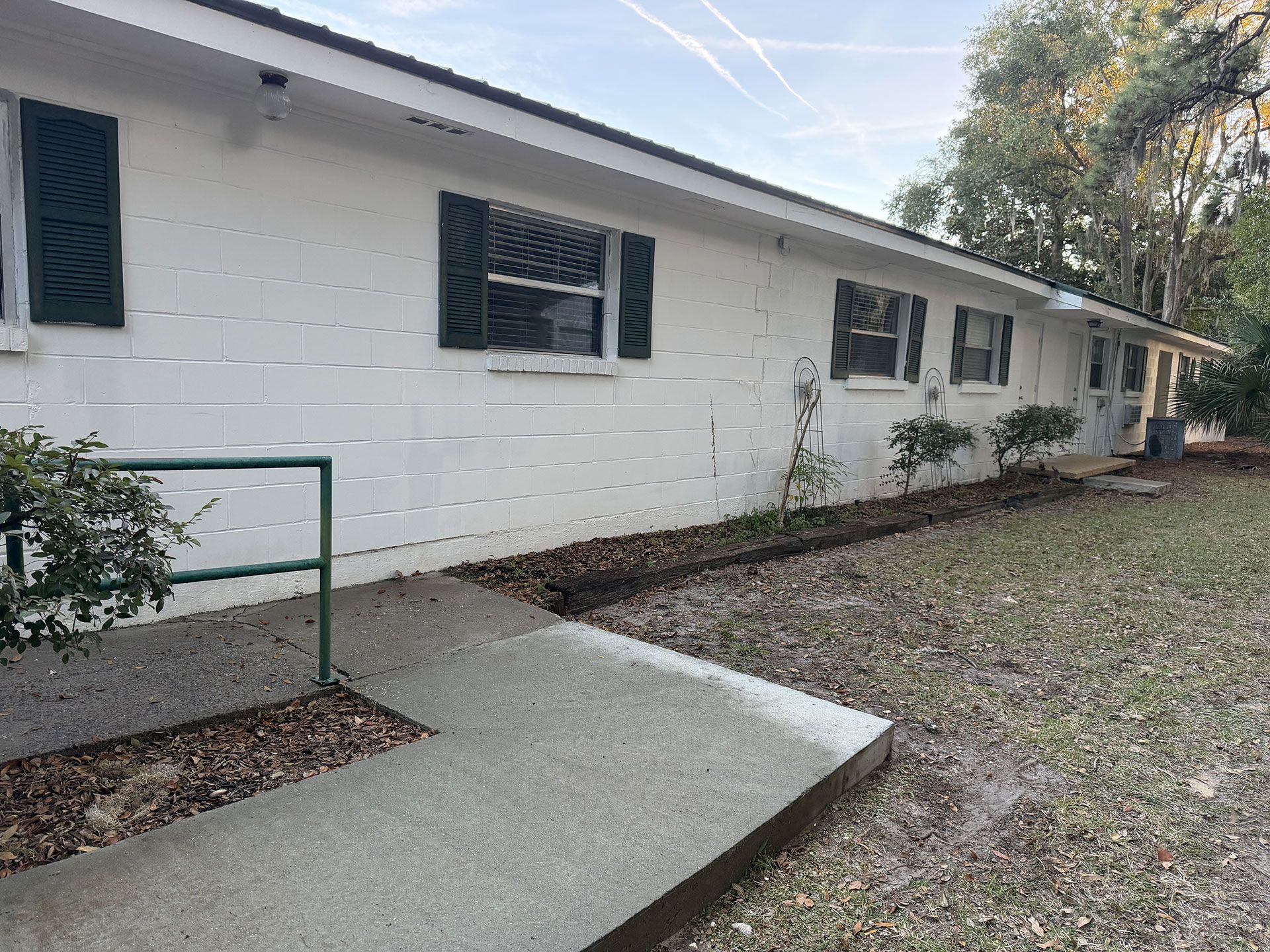 Single-story white house exterior with windows, ramp, and grassy yard.