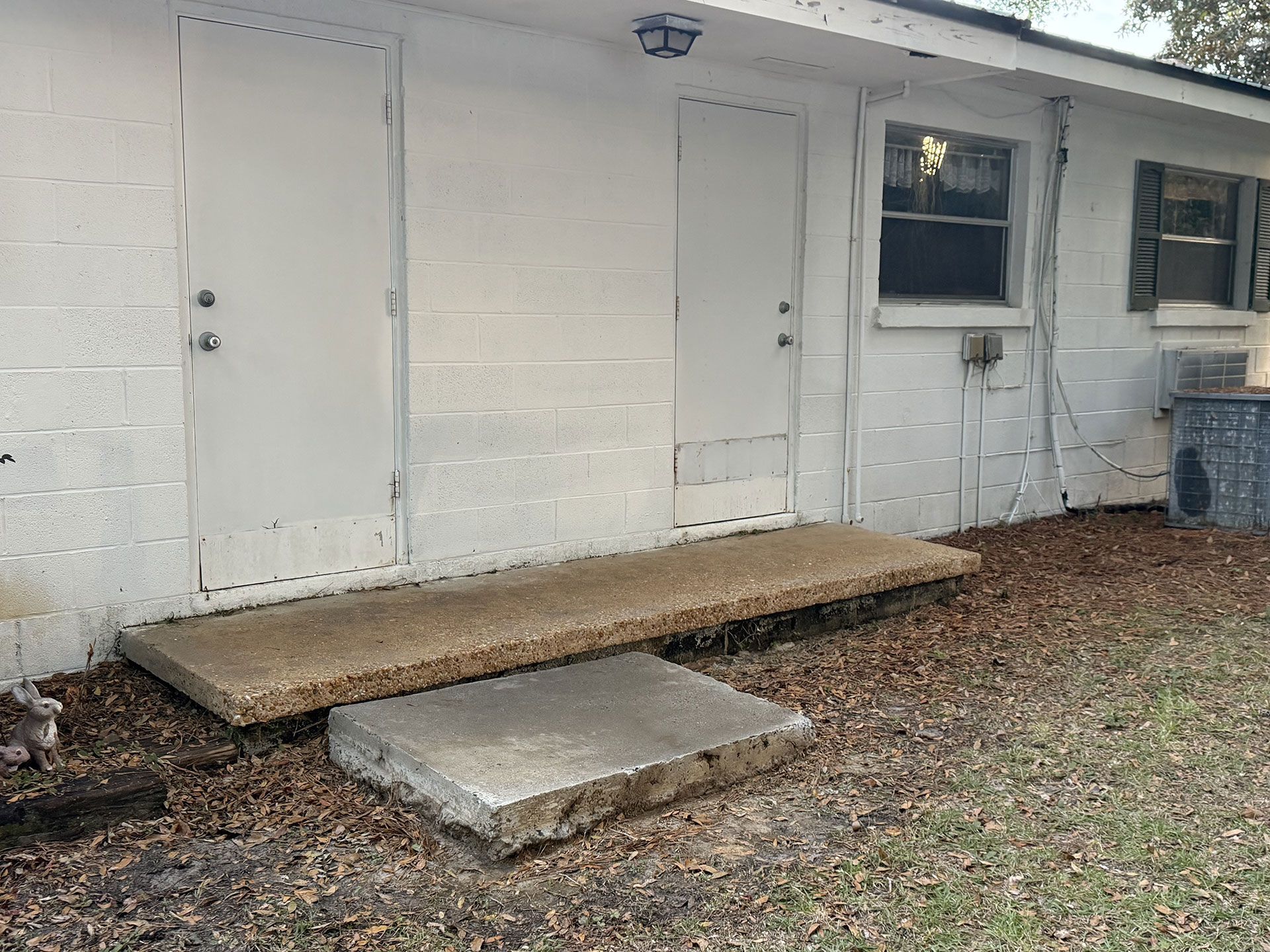 White building exterior with a doorway, window, and a concrete ramp over a gravel yard
