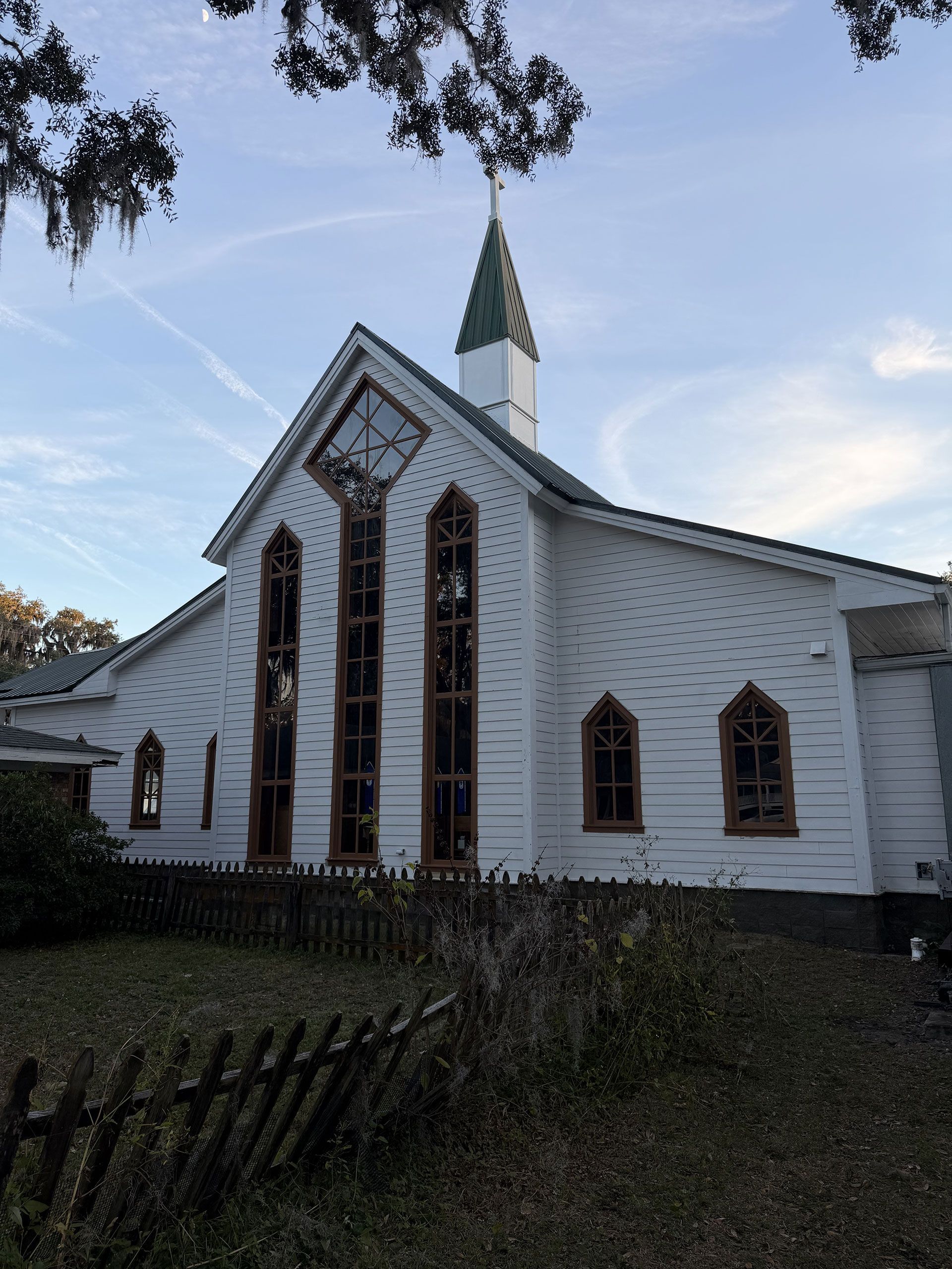White wooden church with tall stained-glass windows and a green steeple under a blue sky