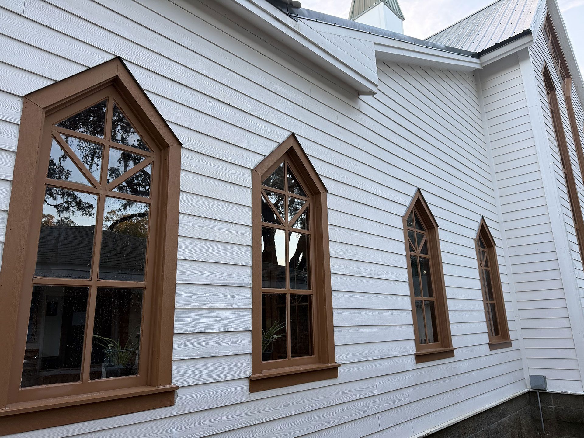 White clapboard church wall with several narrow stained-glass windows framed in brown wood.