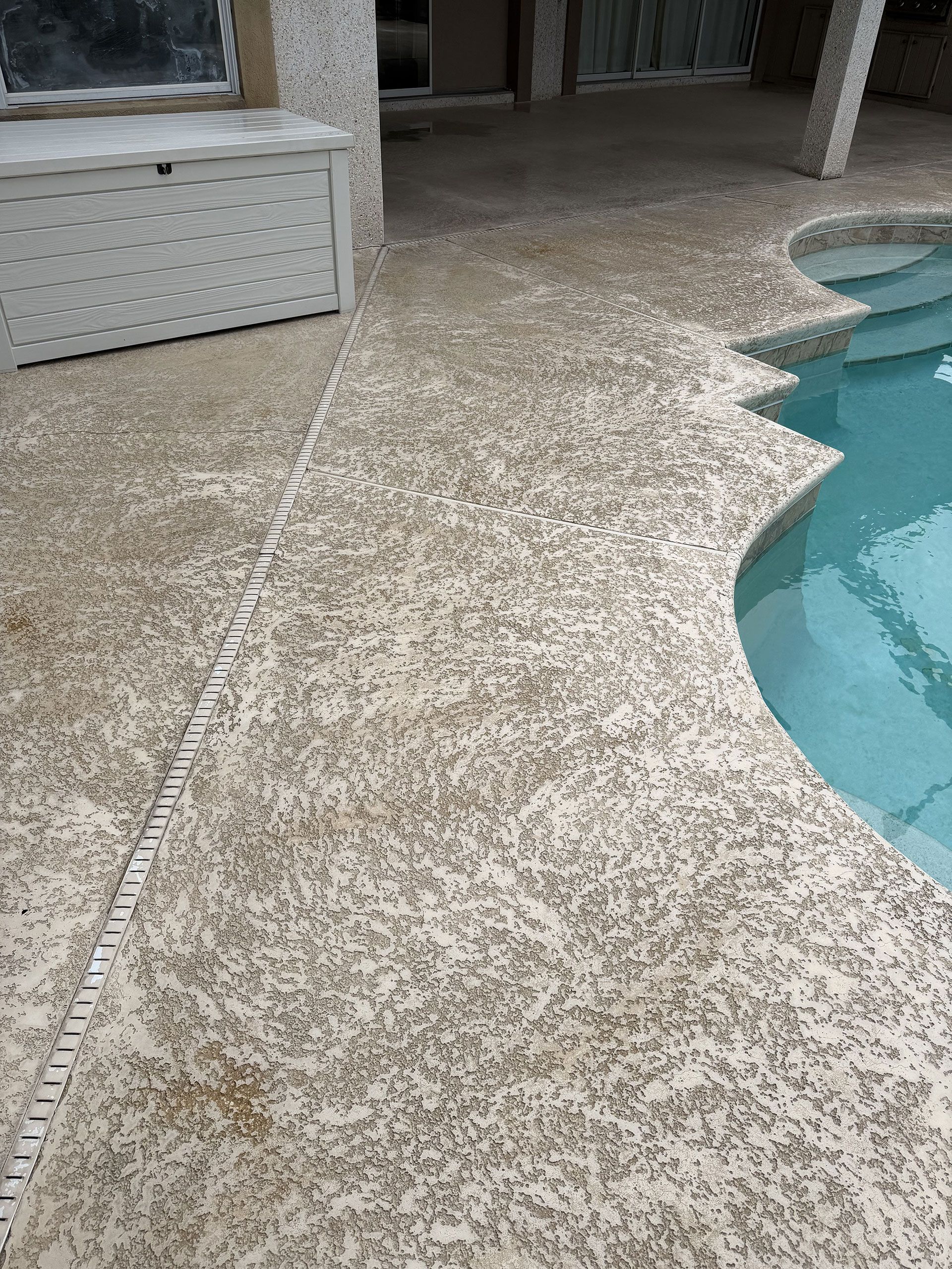 Speckled stone patio beside a curved swimming pool and covered seating area
