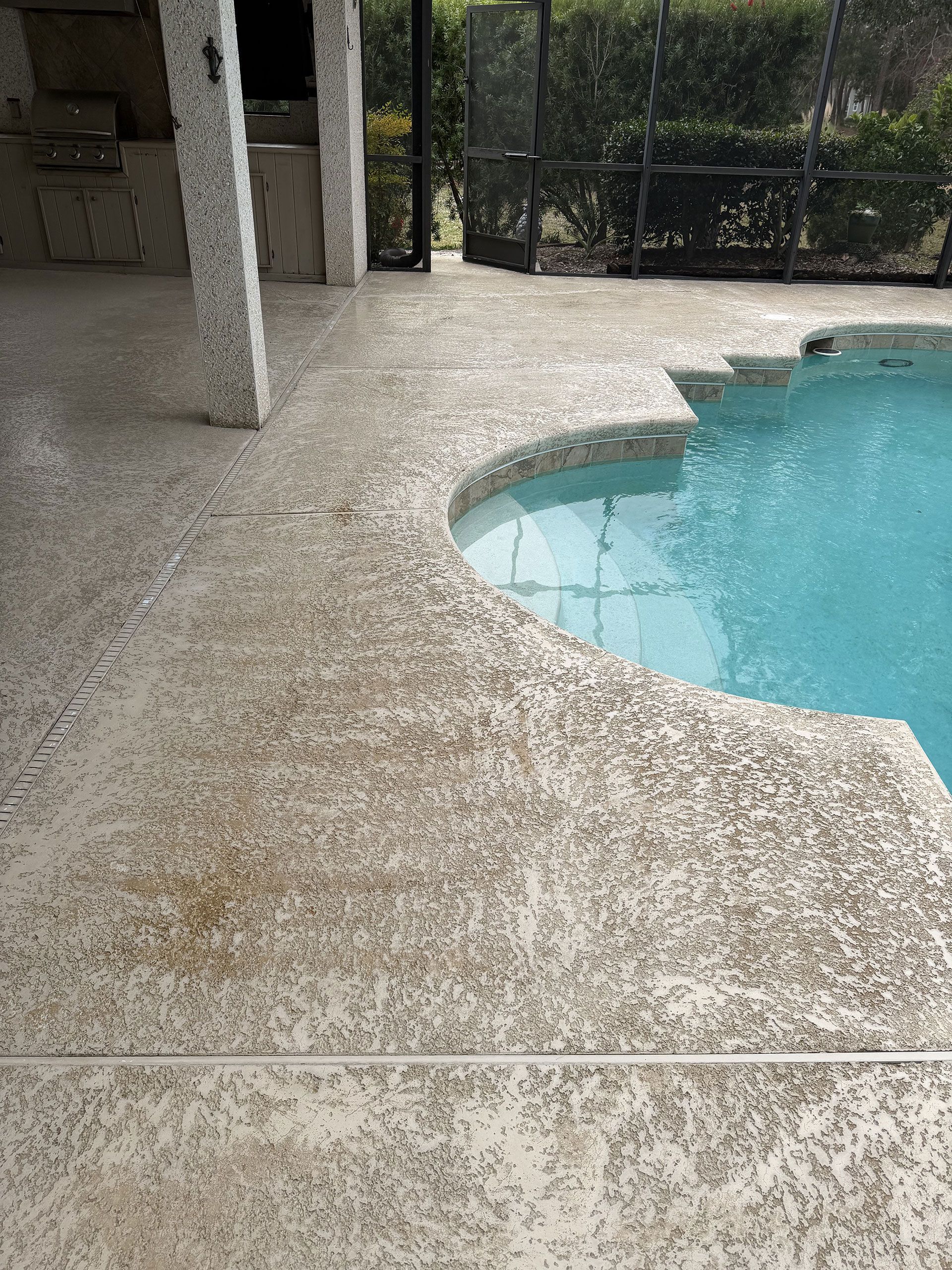 Covered patio beside a backyard swimming pool with speckled stone flooring and a curved pool edge