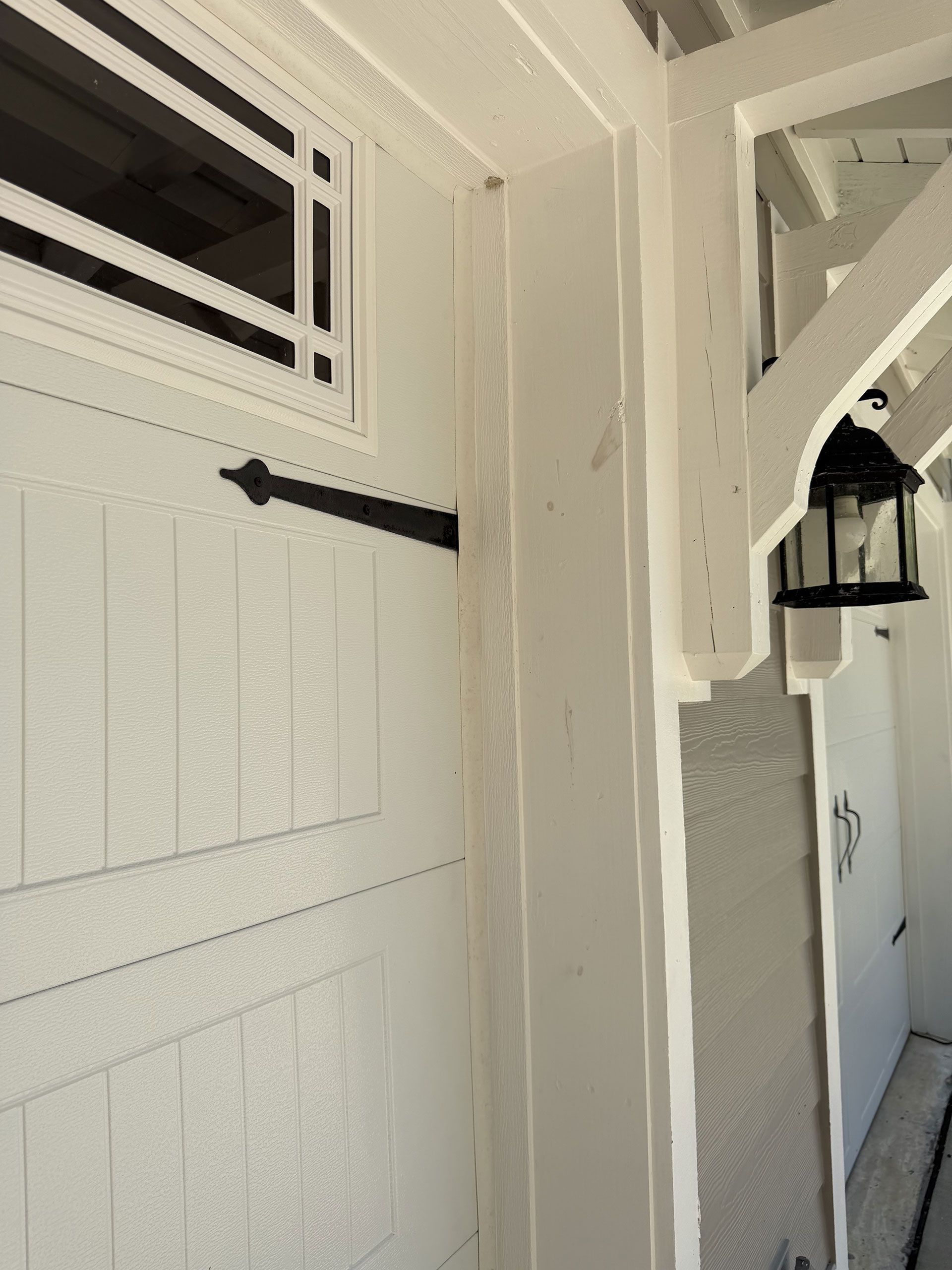 White painted porch with a black lantern and shuttered door in a narrow entryway