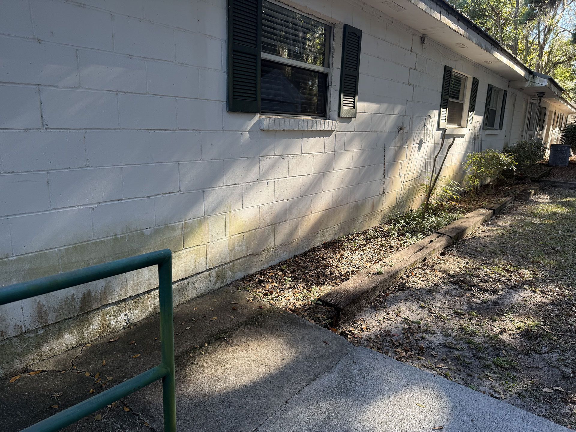 White cinderblock building exterior with windows, along a gravel path beside a green railing