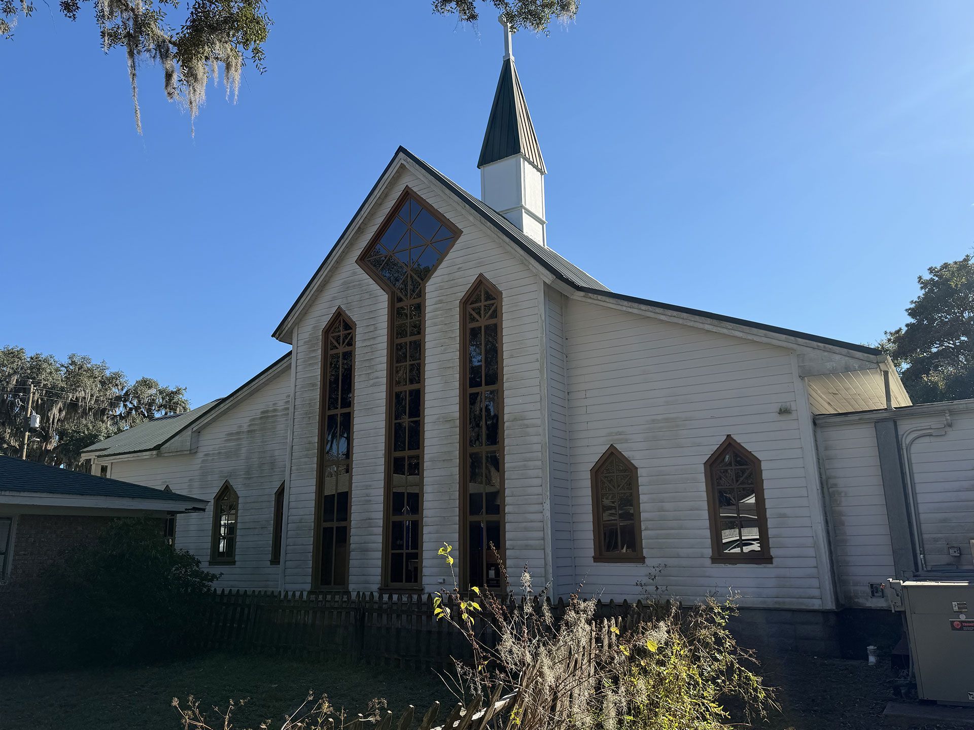 White church with tall stained-glass windows and steeple under a clear blue sky