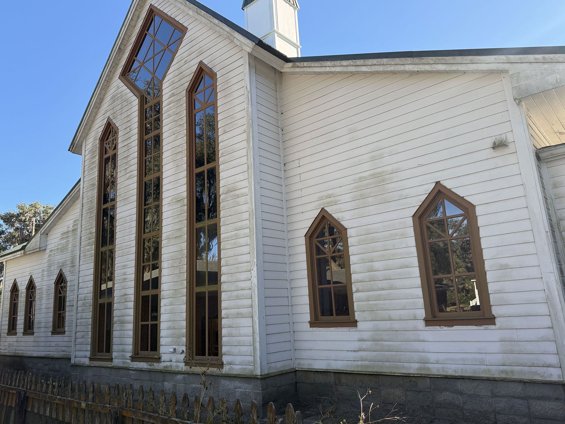 White wooden church exterior with tall stained-glass windows and a steep roof on a sunny day