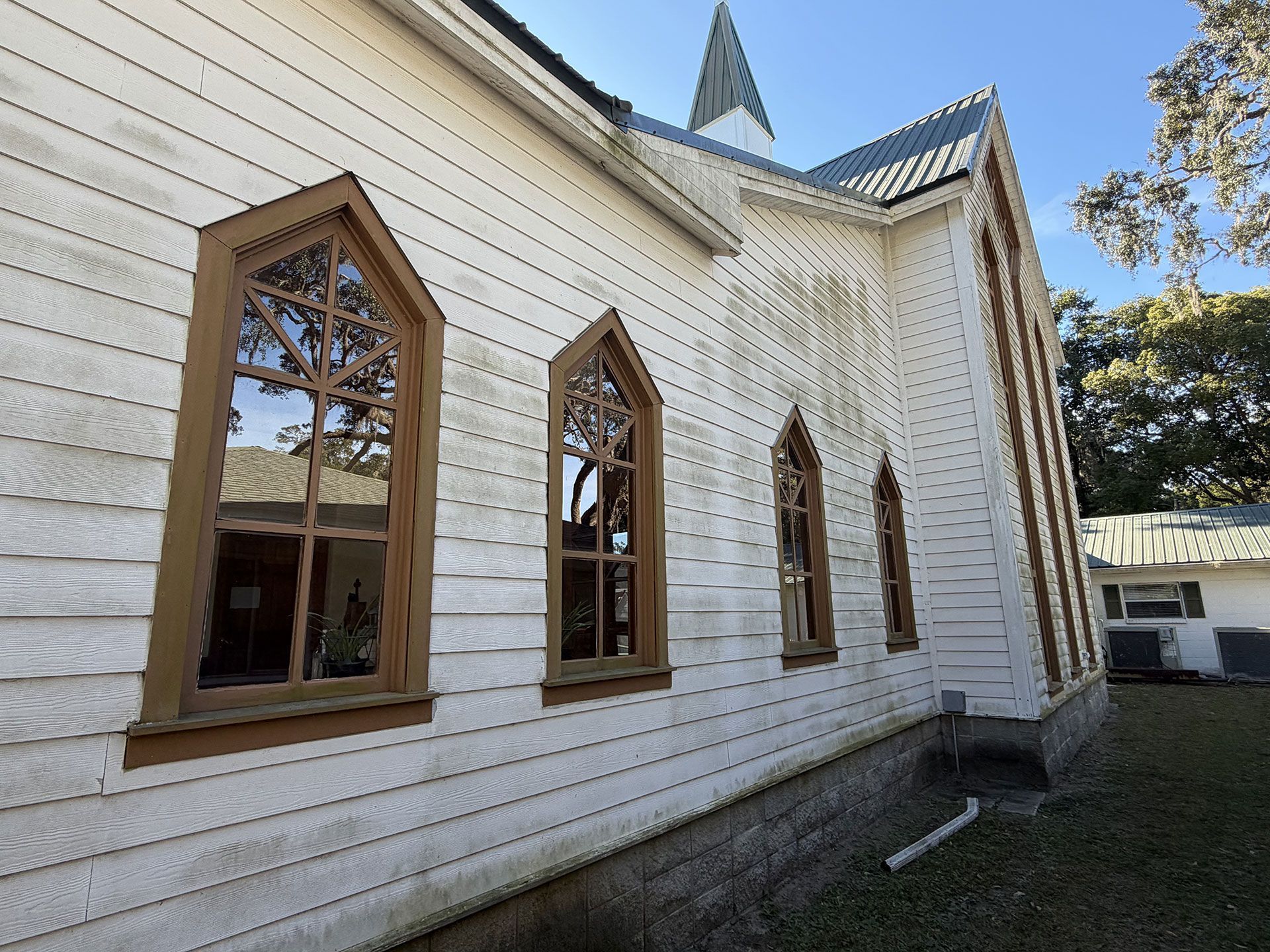 White wooden church exterior with tall arched stained-glass windows and a small steeple.