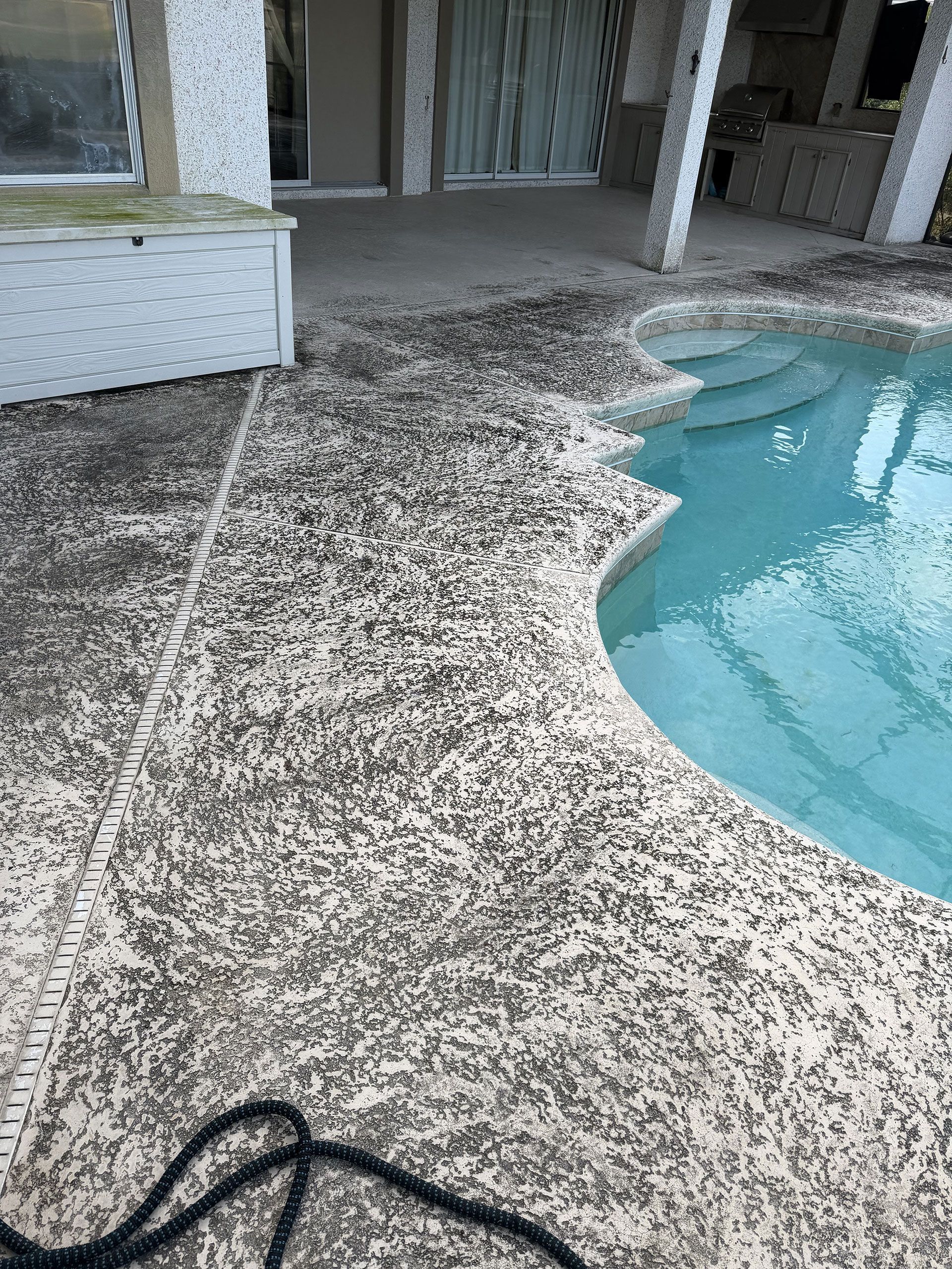 Pebble-finish patio beside a blue swimming pool and screened porch.