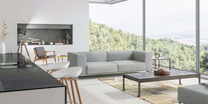 Modern living room with gray sofa, wooden chairs, and floor-to-ceiling windows overlooking greenery