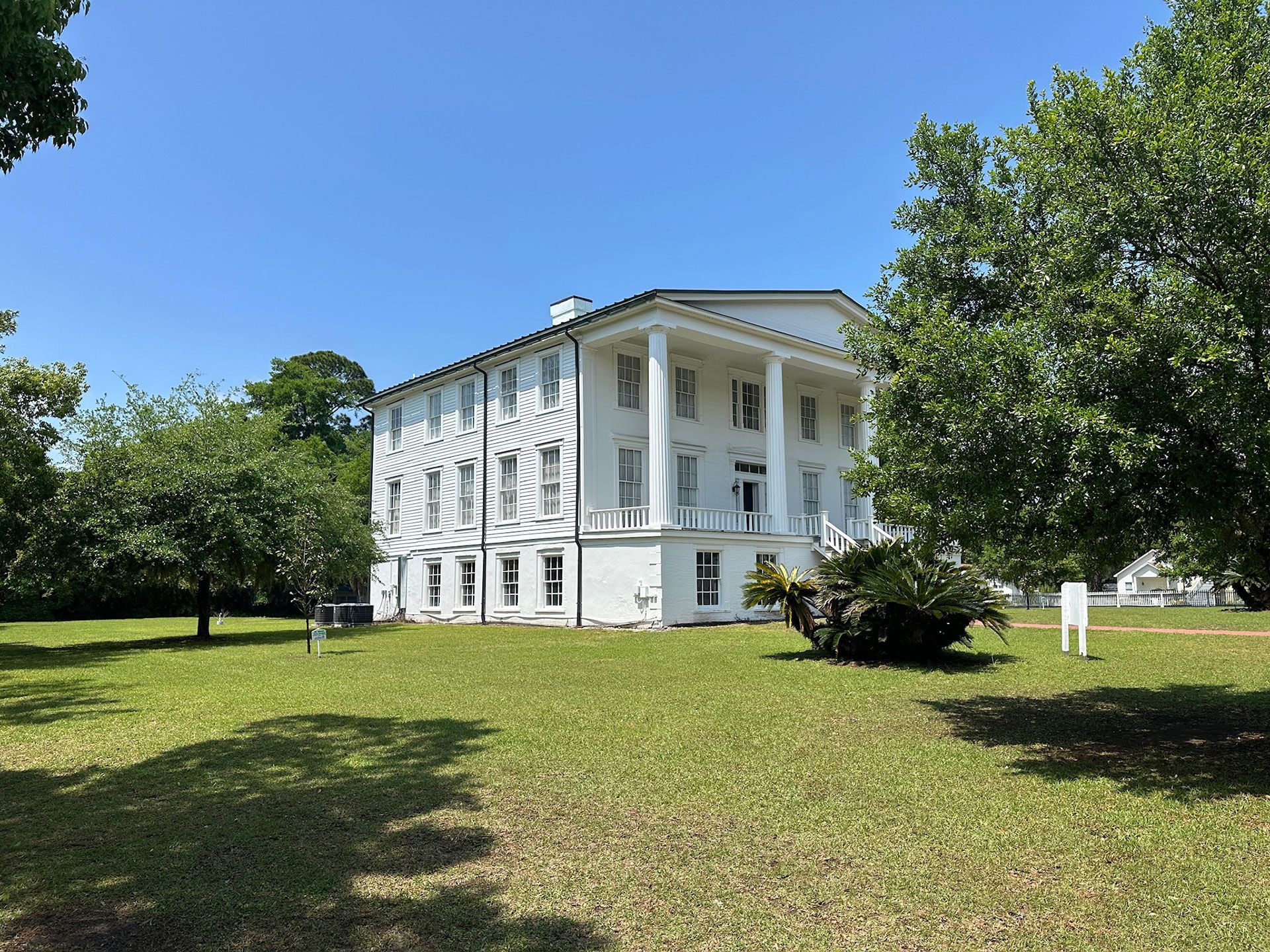 White historic house with columns on a grassy lawn under a clear blue sky