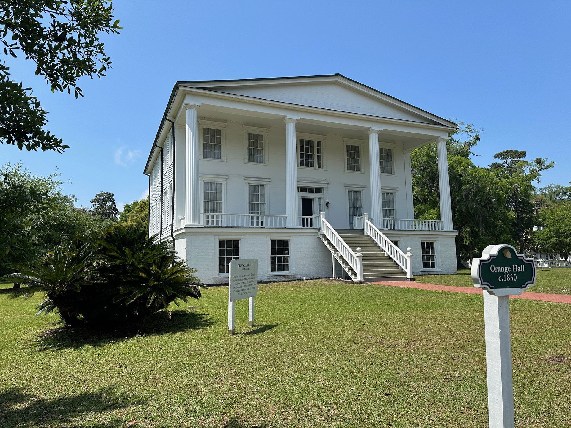 White historic house with columns and front steps on a grassy lawn under a blue sky