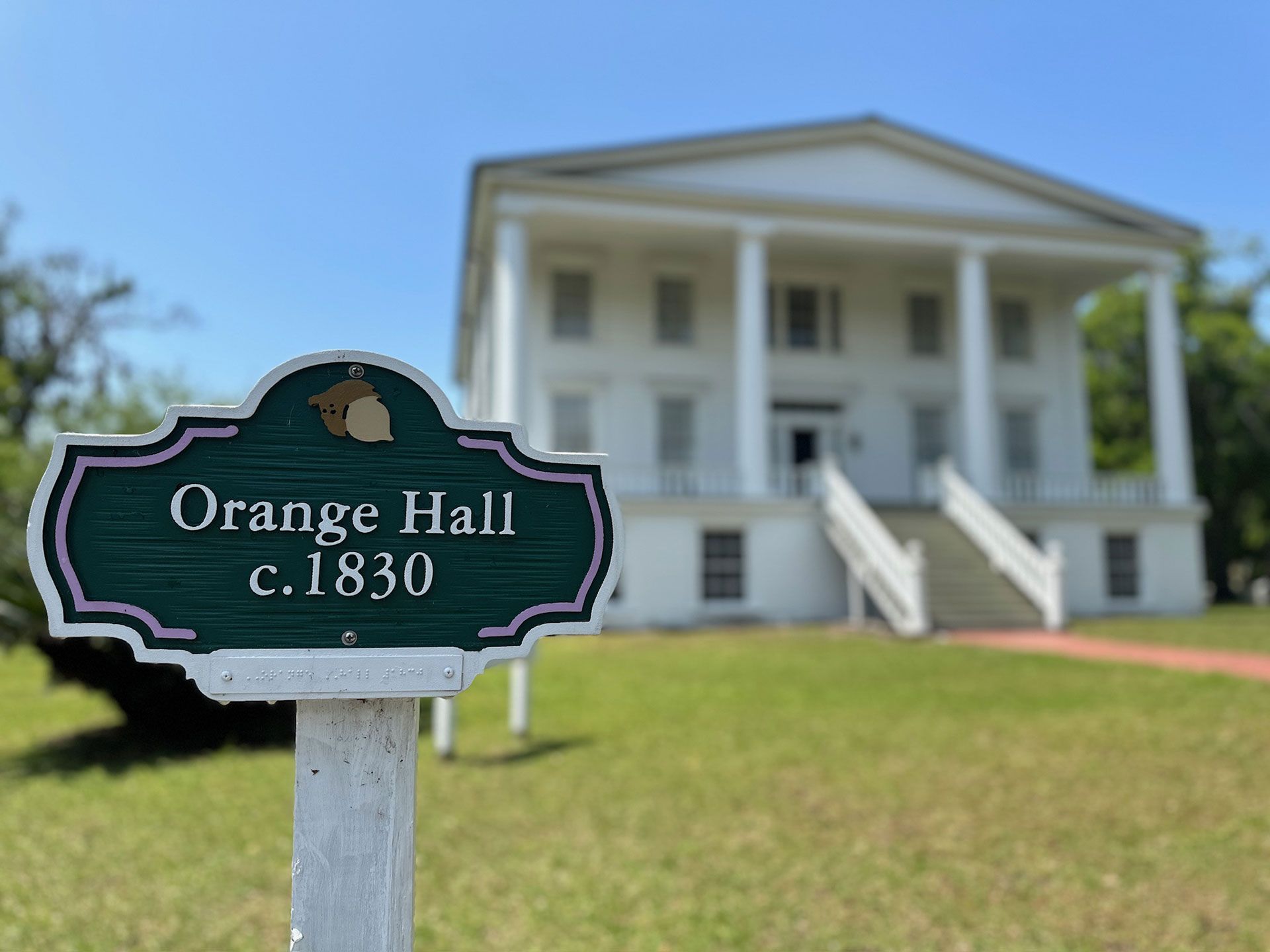 Orange Hall historic house with sign reading “c. 1830” in front of white columns and a grassy lawn.