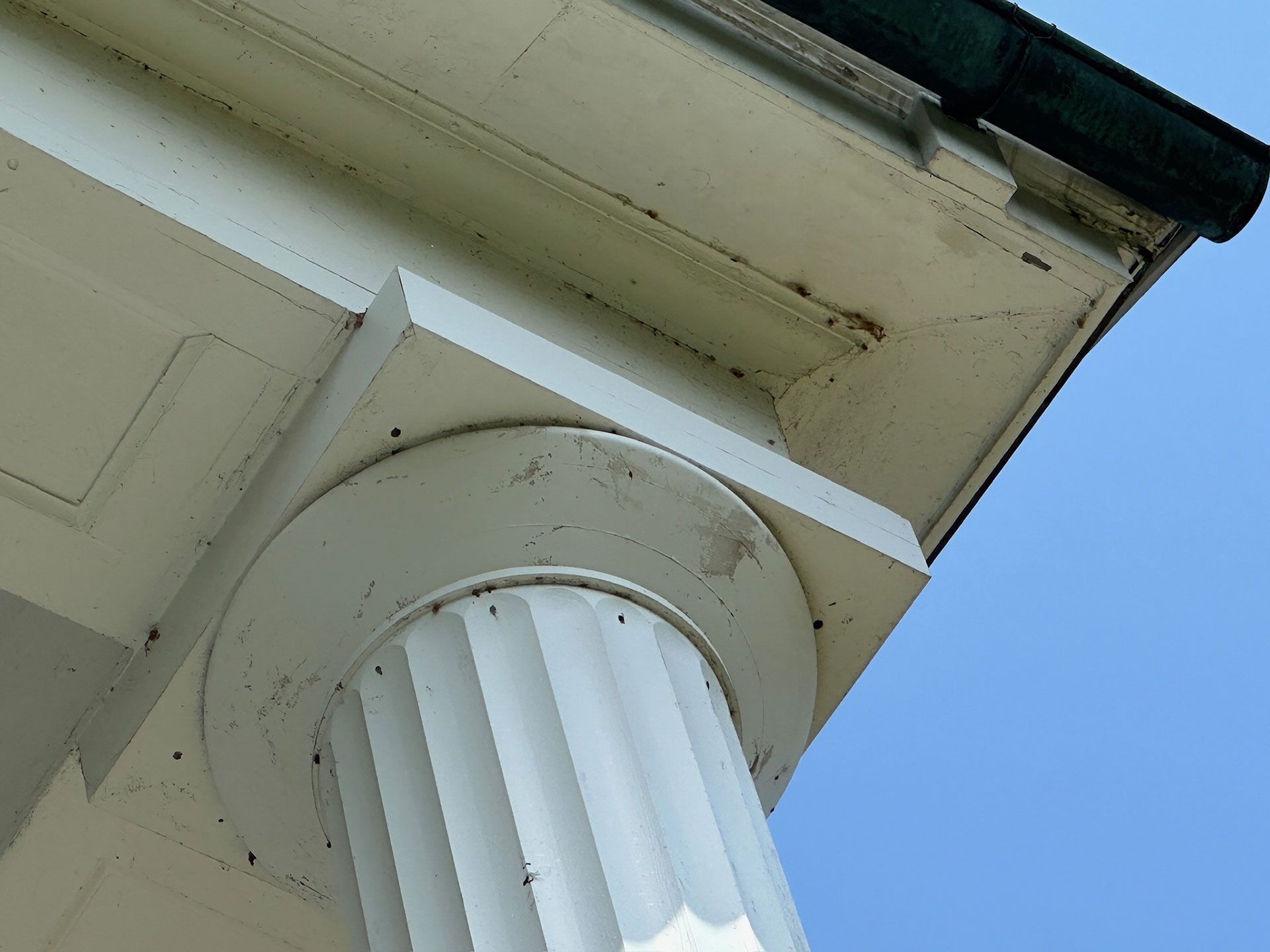 Close-up of a white building column and eaves against a blue sky.