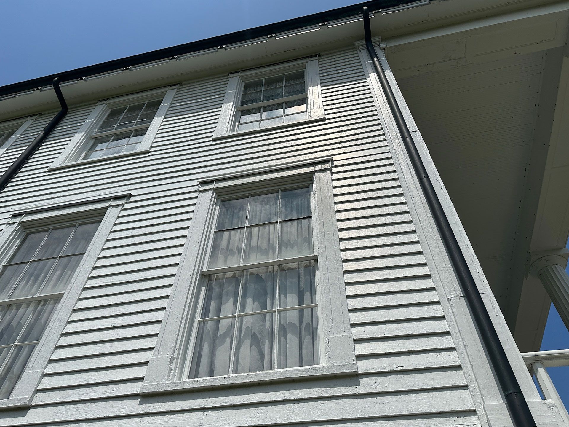 Low-angle view of a white house exterior with tall windows and gray siding under the roof eaves