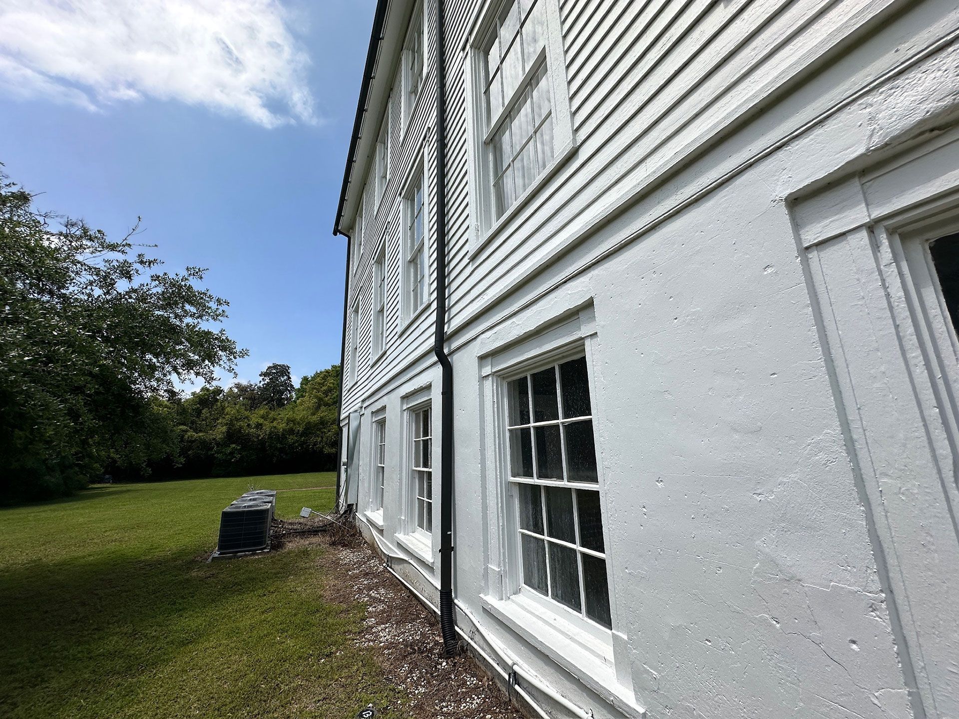 White clapboard house exterior with windows beside a grassy yard and trees under a blue sky