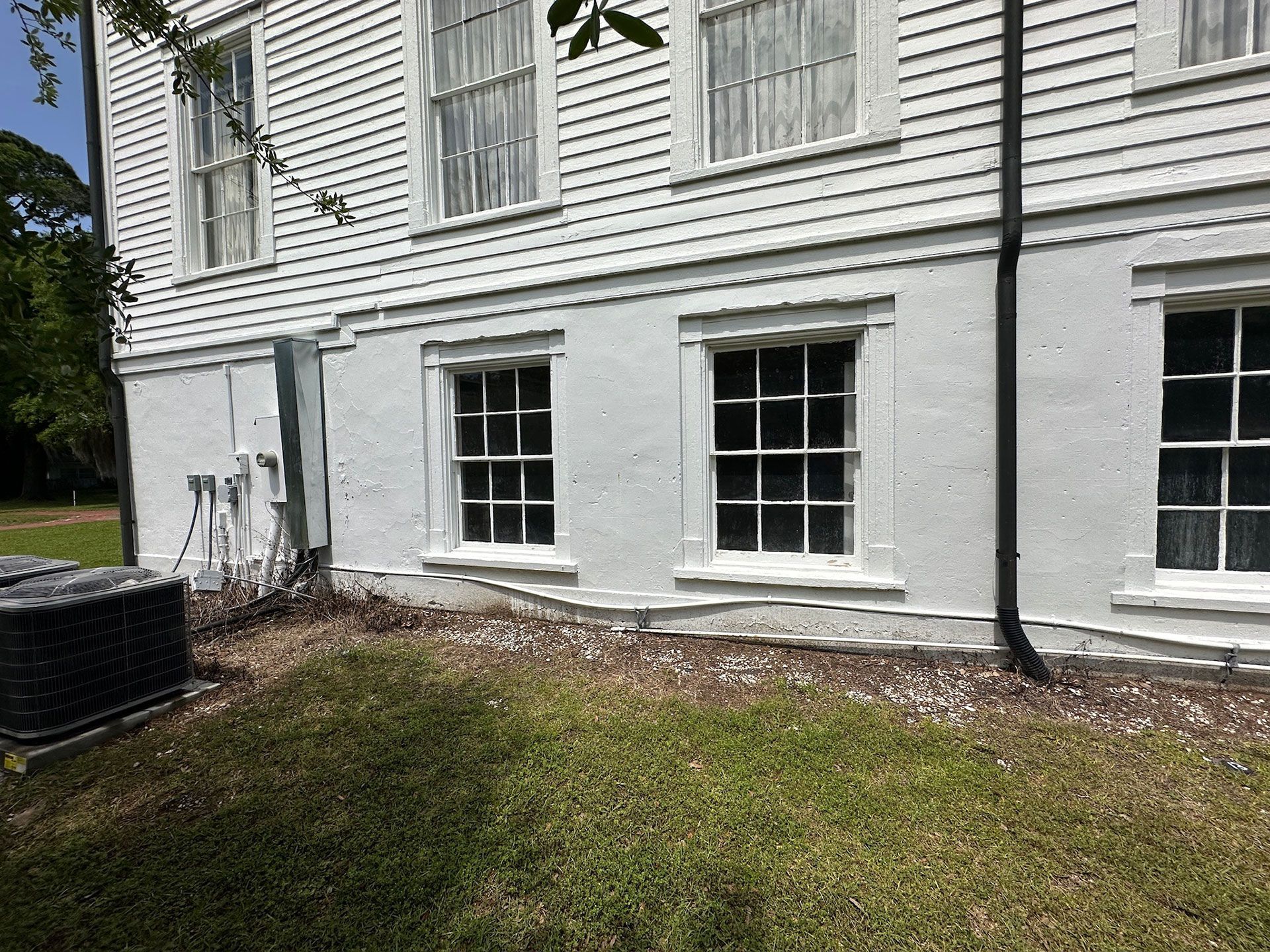 White house exterior with basement windows, black downspout, and grass yard along the foundation