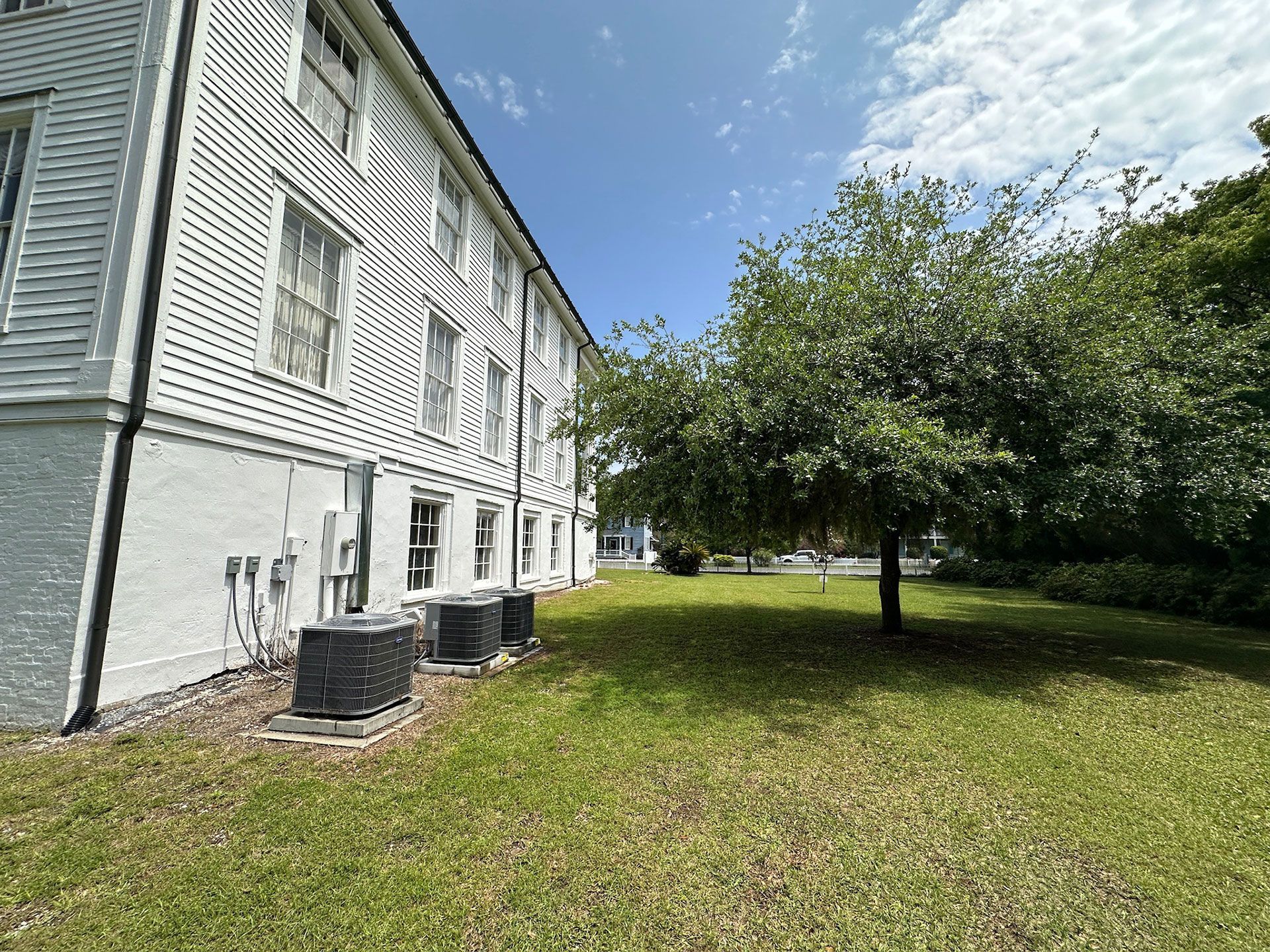 White apartment building beside a grassy yard and tree under a blue sky