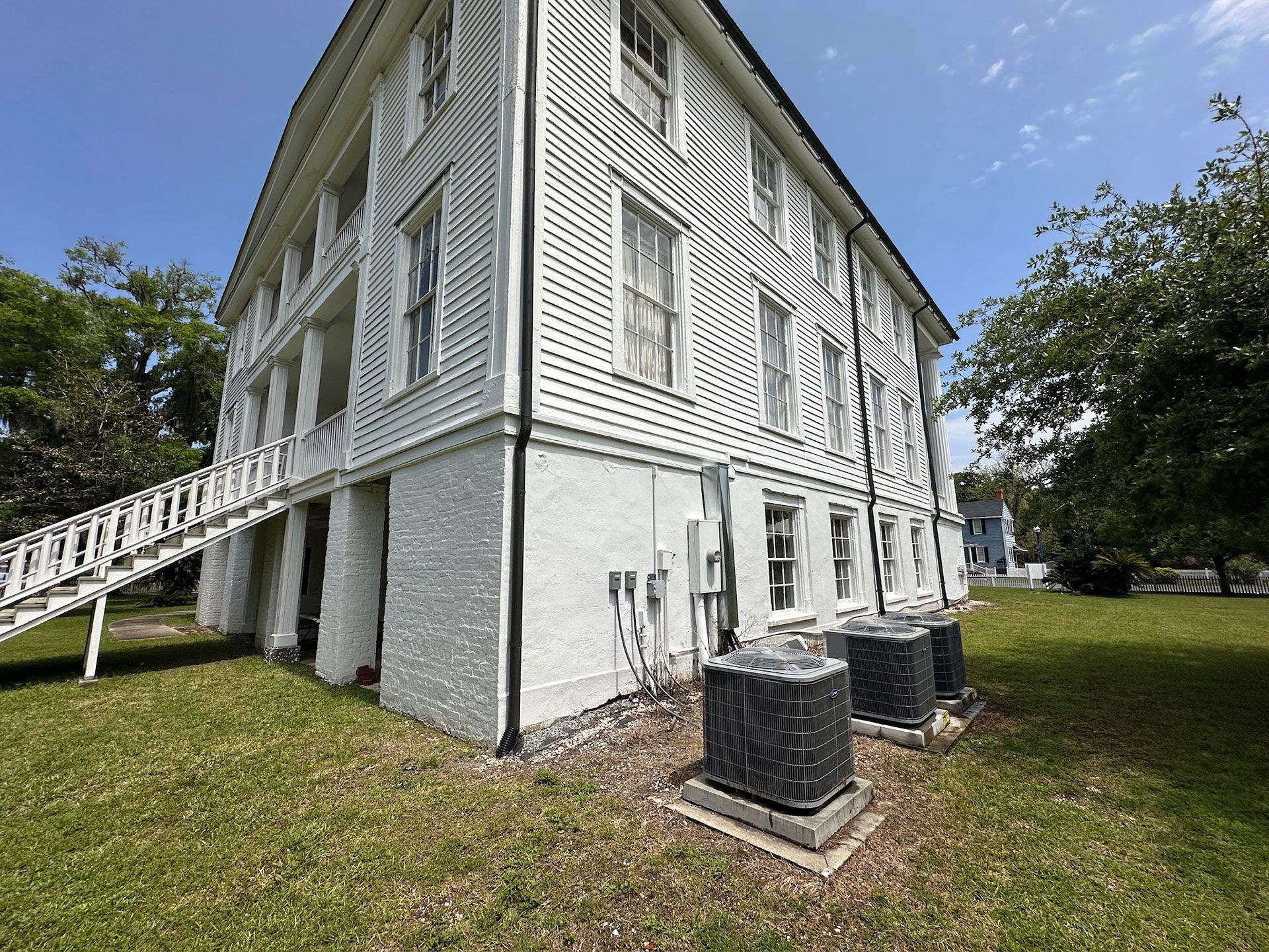 White historic house with porch and steps on a grassy lawn under a blue sky