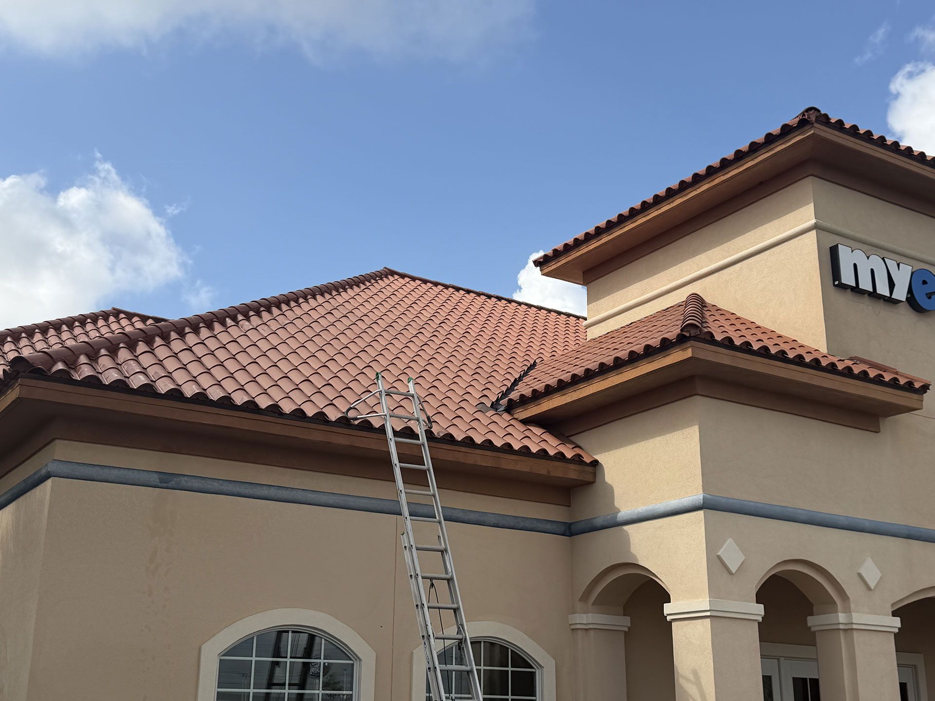 Ladder leaning against a beige house with a red tile roof under a blue sky