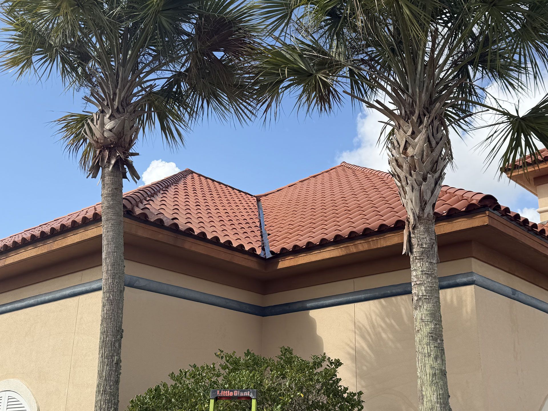 Tan house with red tile roof and palm trees against a blue sky