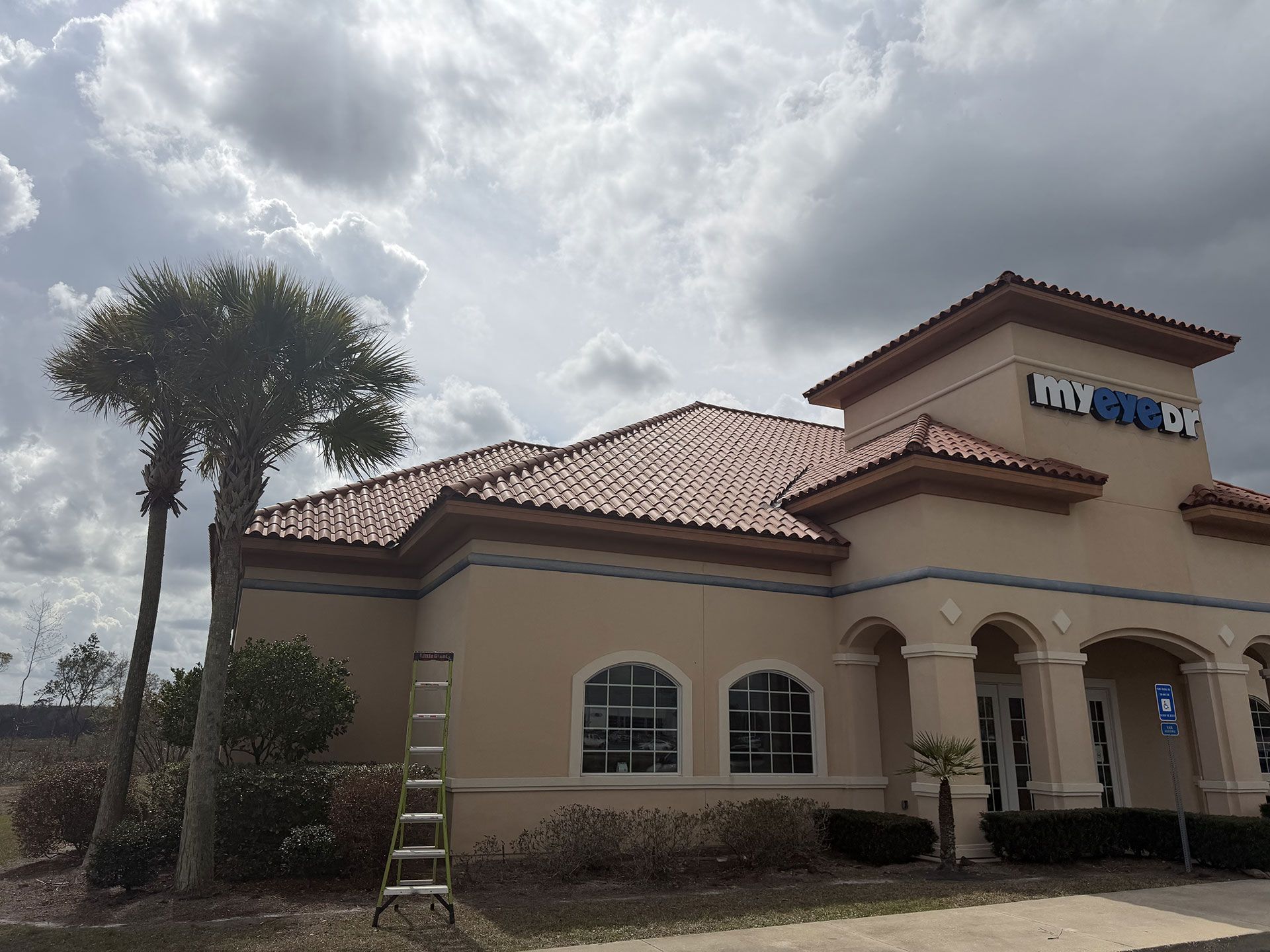Spanish-style bank building with tan stucco walls, red tile roof, and palm tree under cloudy sky