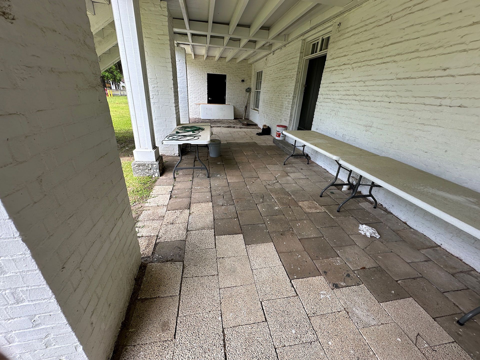 Covered brick porch with benches and a small table along a white-painted wall.