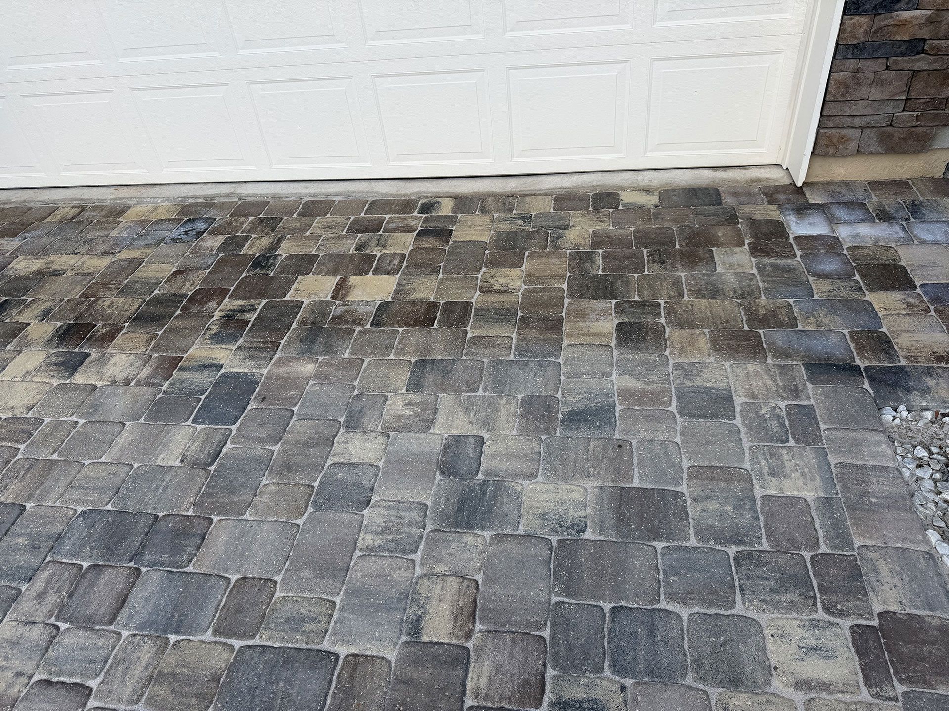 Stone-paver driveway leading to a white garage door with dark tire stains near the entrance