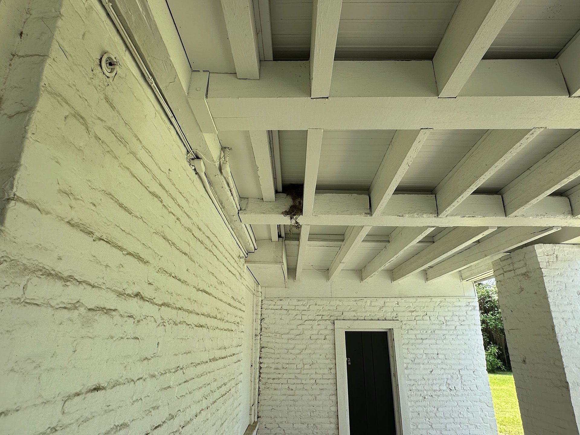 Covered porch with white painted beams and brick wall, showing an open doorway to the outside.