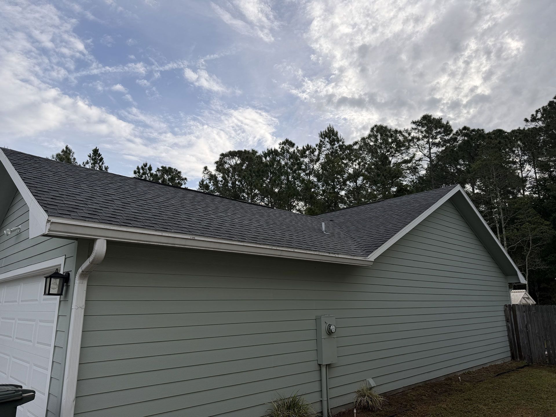 Gray house exterior with wavy roof shingles, viewed from the side under a cloudy sky