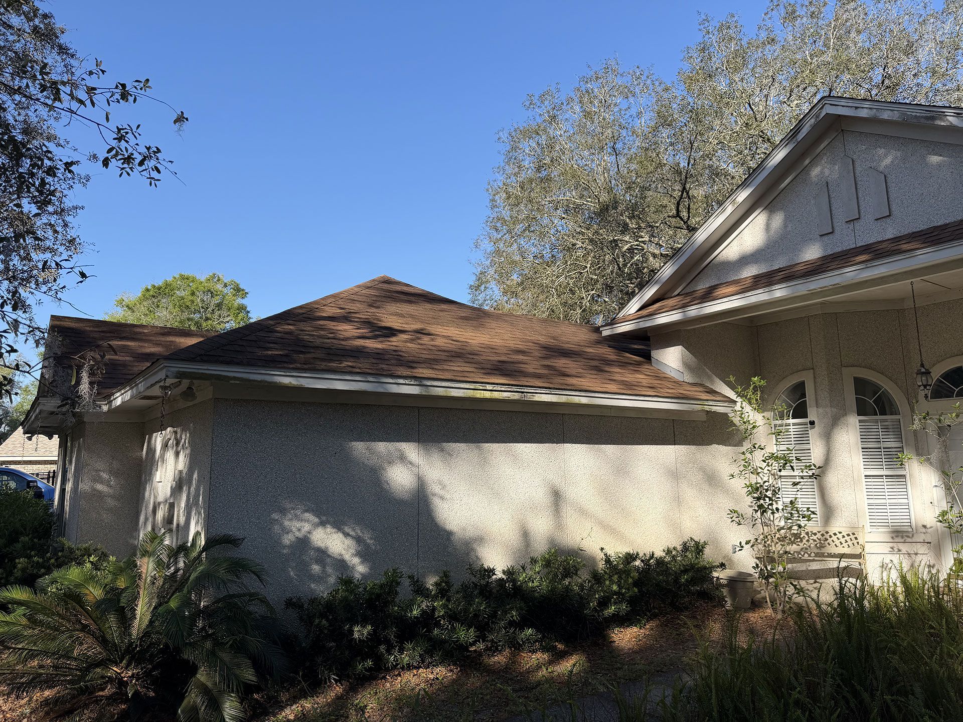 Single-story house with tan stucco walls, brown roof, and arched porch under a blue sky