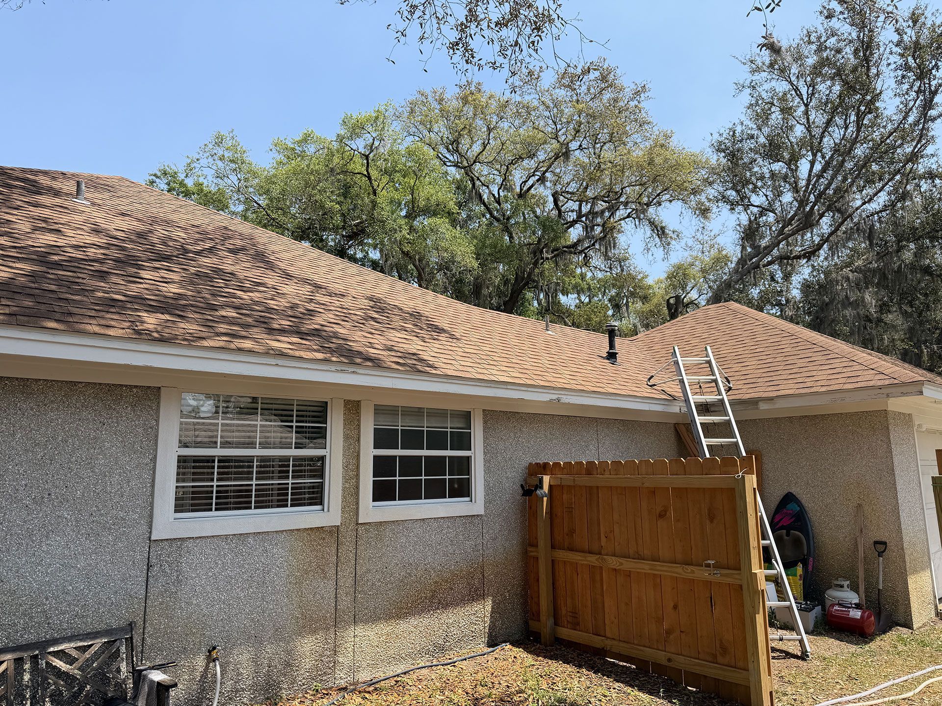 Roof repairs on a house, with a ladder leaning against the roof and a wooden fence below.