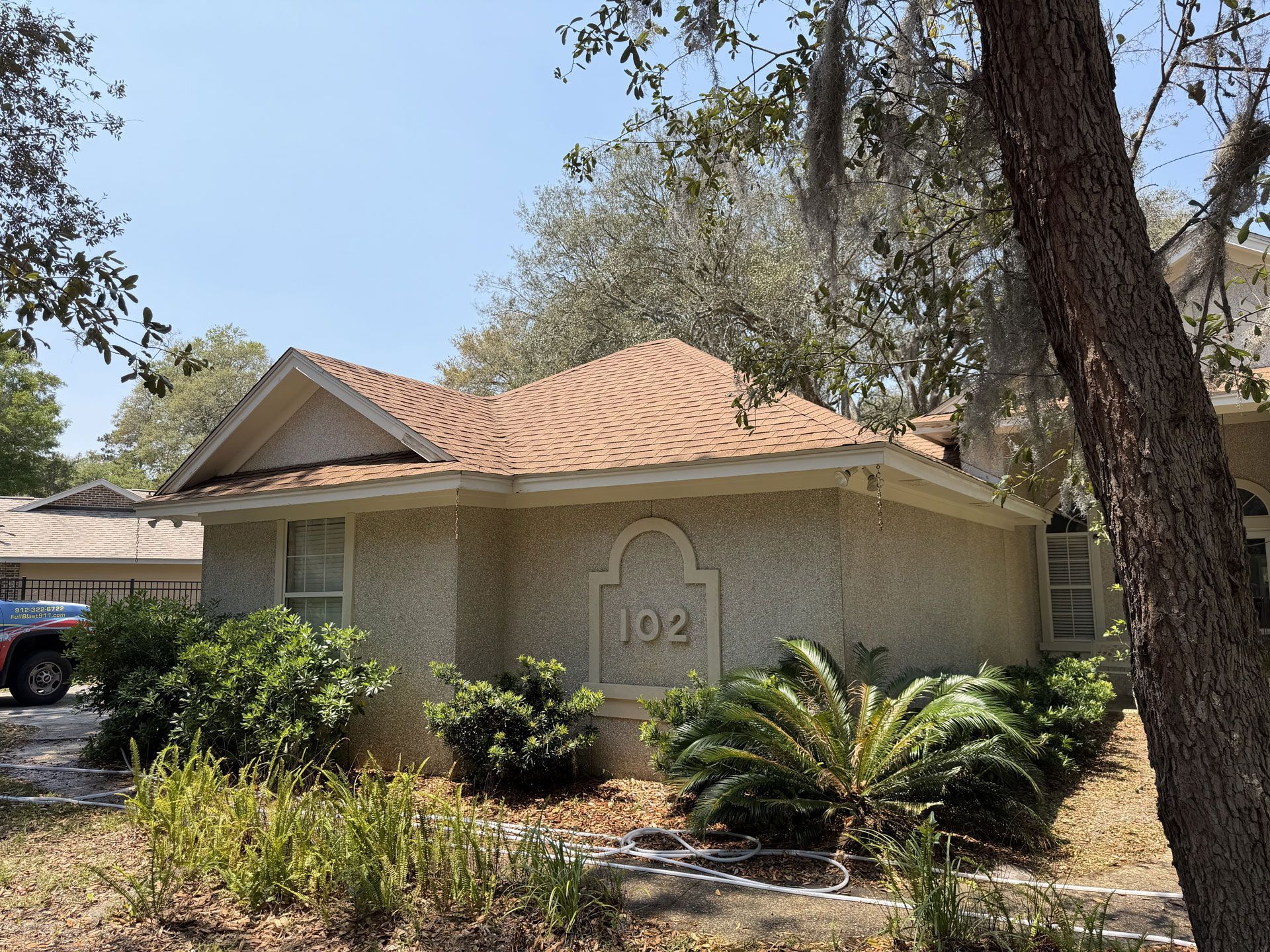 Single-story beige house with orange tile roof, front shrubs, and trees in a sunny yard
