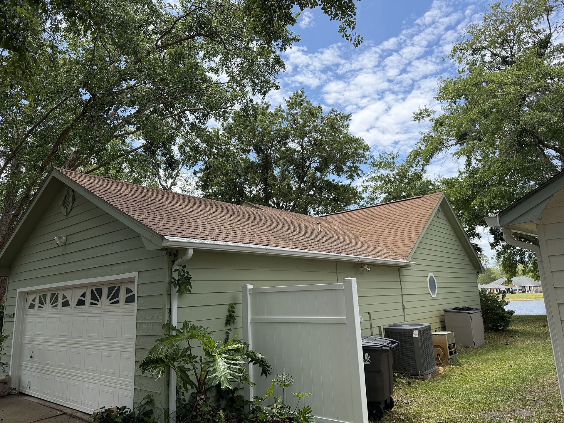 Light green detached garage with tan roof and white doors, surrounded by trees in a yard.