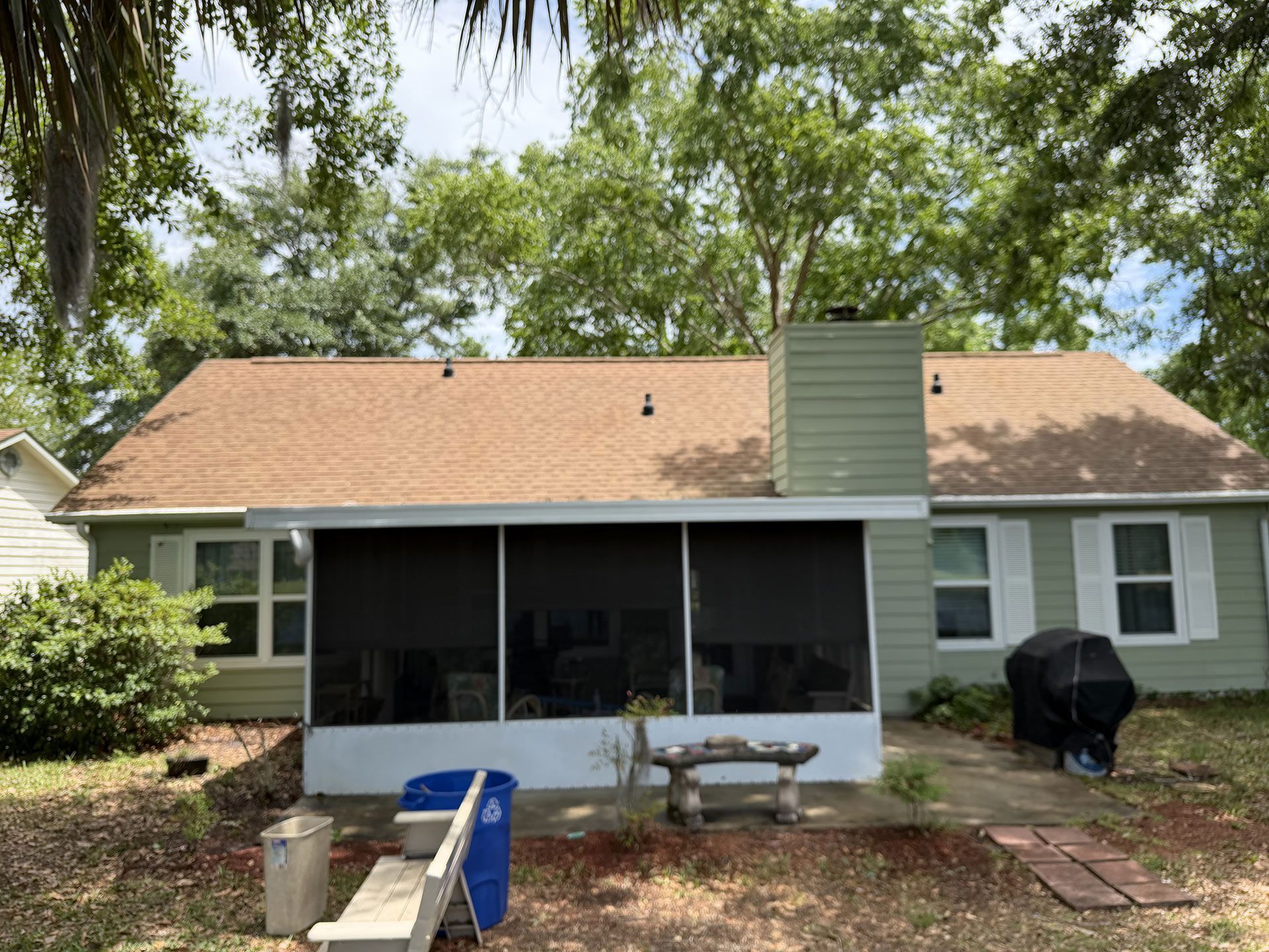 Backyard view of a house with a screened porch, patio furniture, and trees overhead