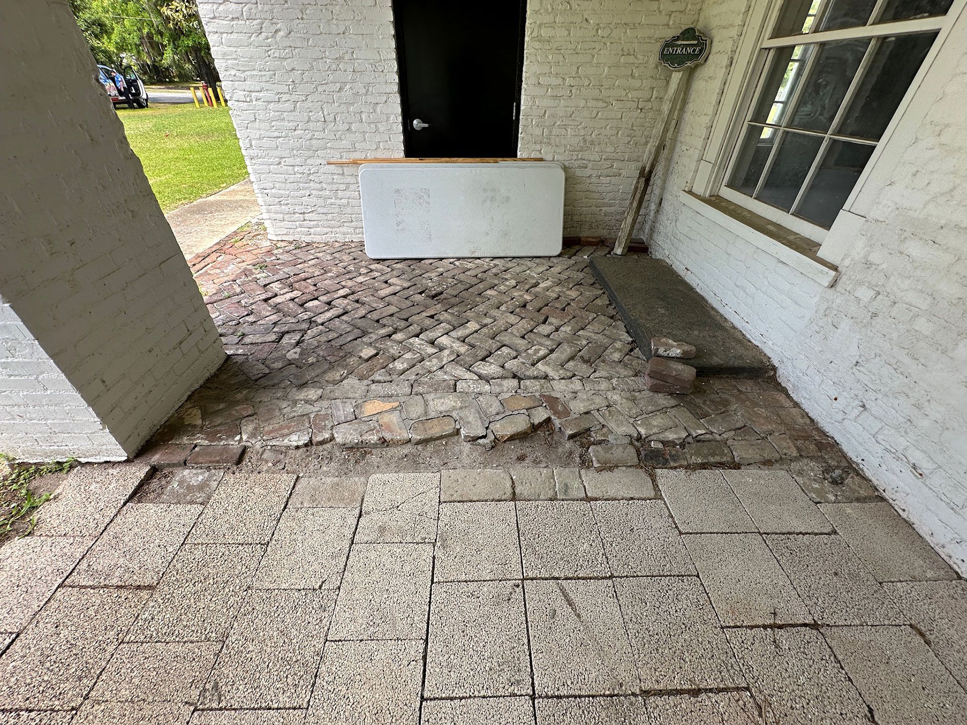 Damaged stone patio beside a white house porch with cracked and uneven paving.