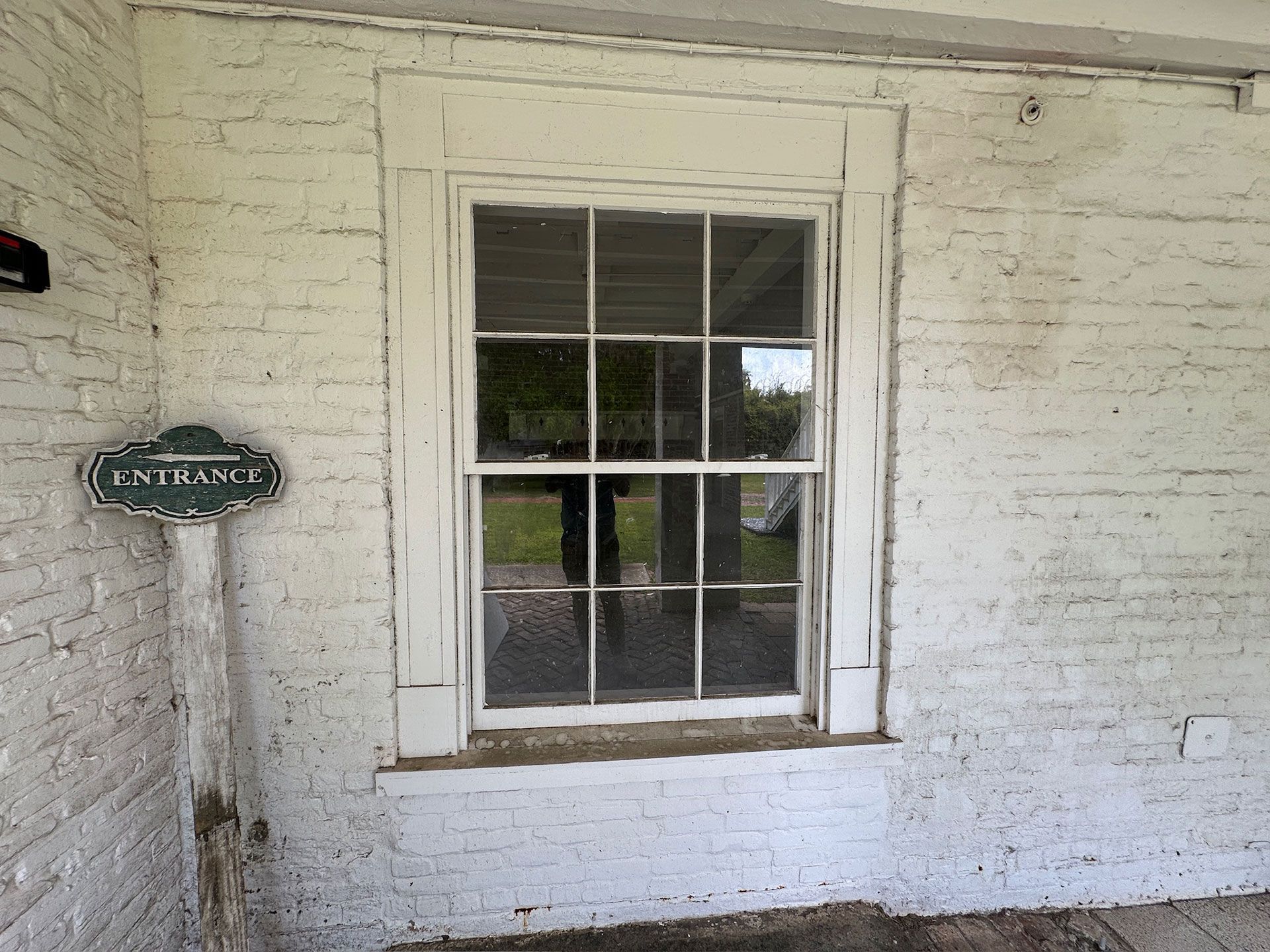 White brick wall with a small window and a green sign mounted beside it