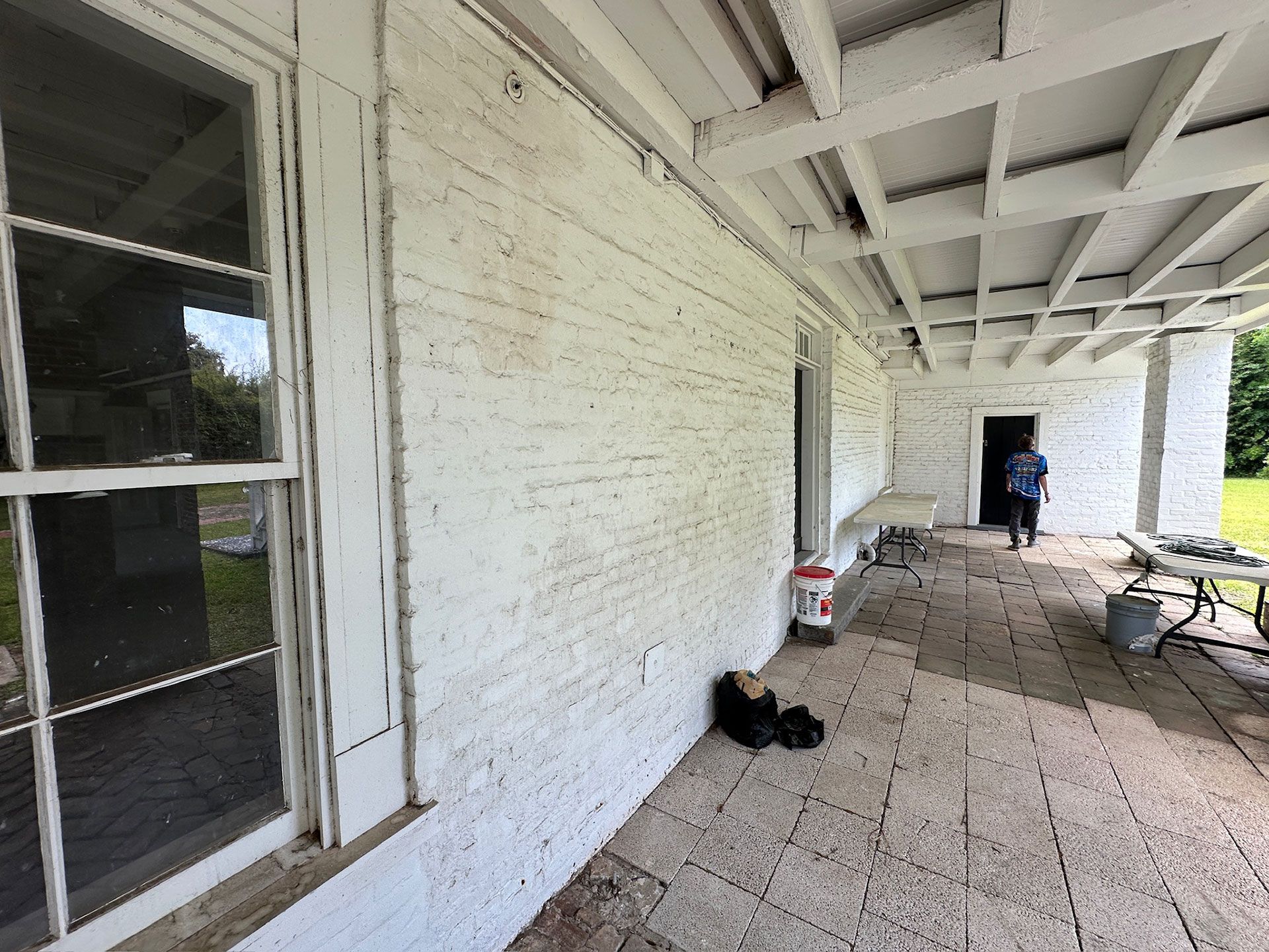 Covered porch with white brick wall, windows, and a person standing near folding chairs at the far end